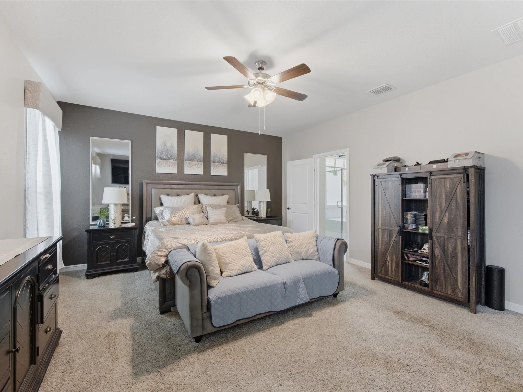 Spacious bedroom on first floor, featuring plush carpet flooring, a dark accent wall, and a ceiling fan with integrated lighting