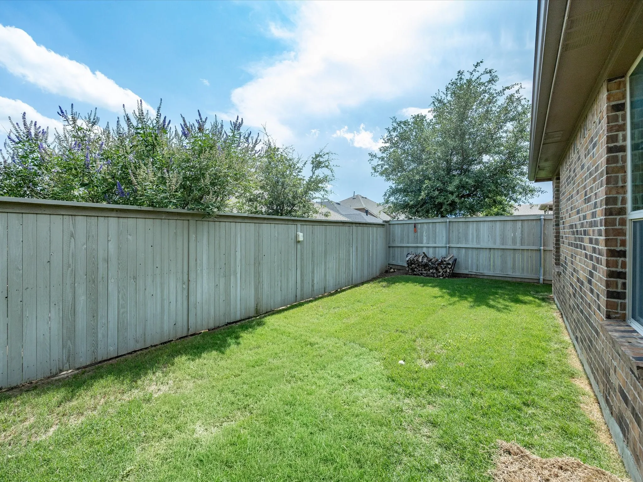 Landscaped backyard featuring a grass lawn, wood privacy fencing, and mature trees