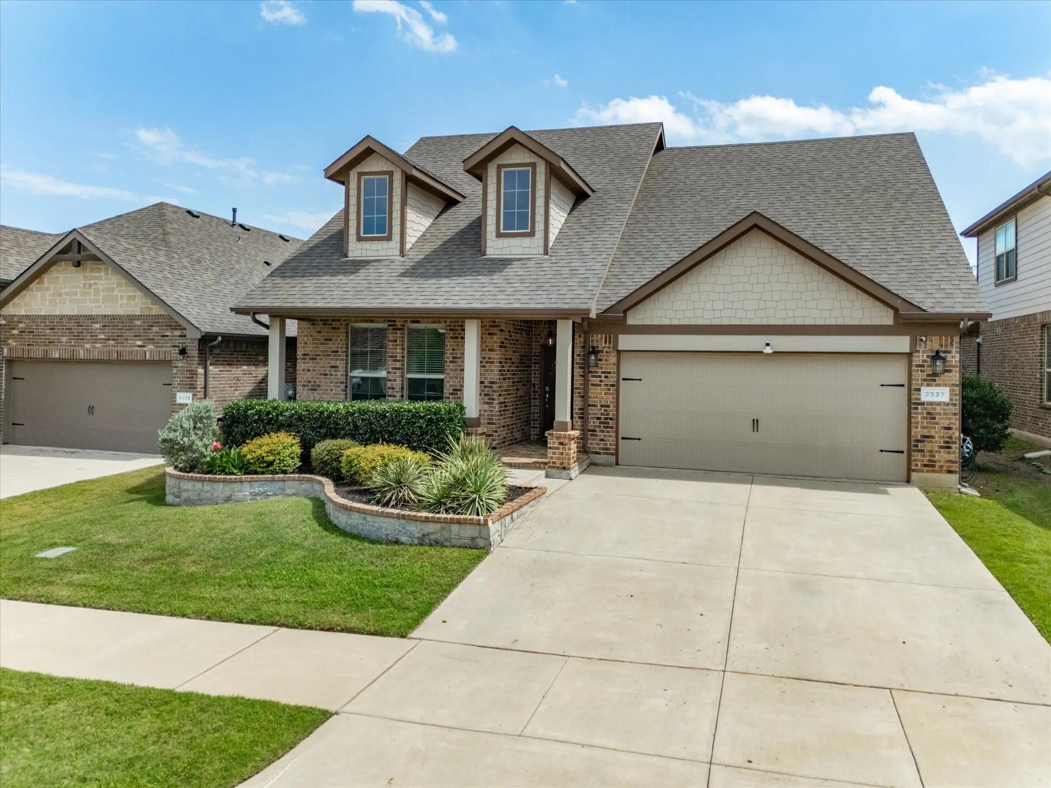Brick and siding exterior featuring a two-car garage, dormer windows, and a manicured front lawn