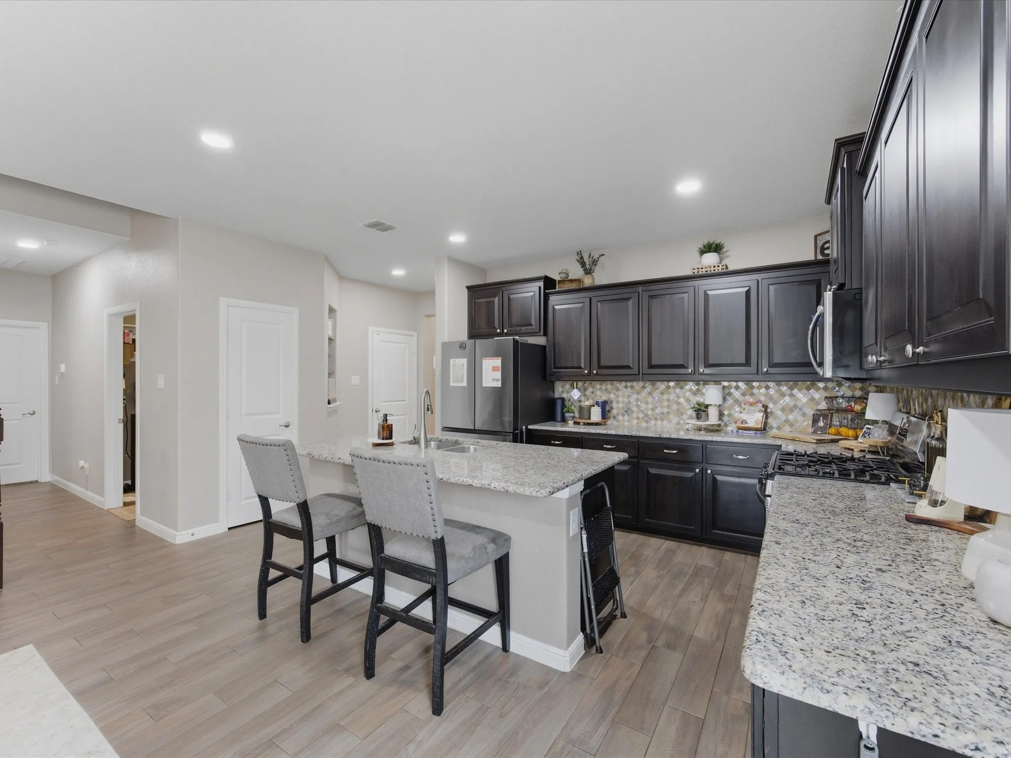 Kitchen featuring dark cabinetry, light-toned granite countertops, a mosaic tile backsplash, and wood-finish flooring