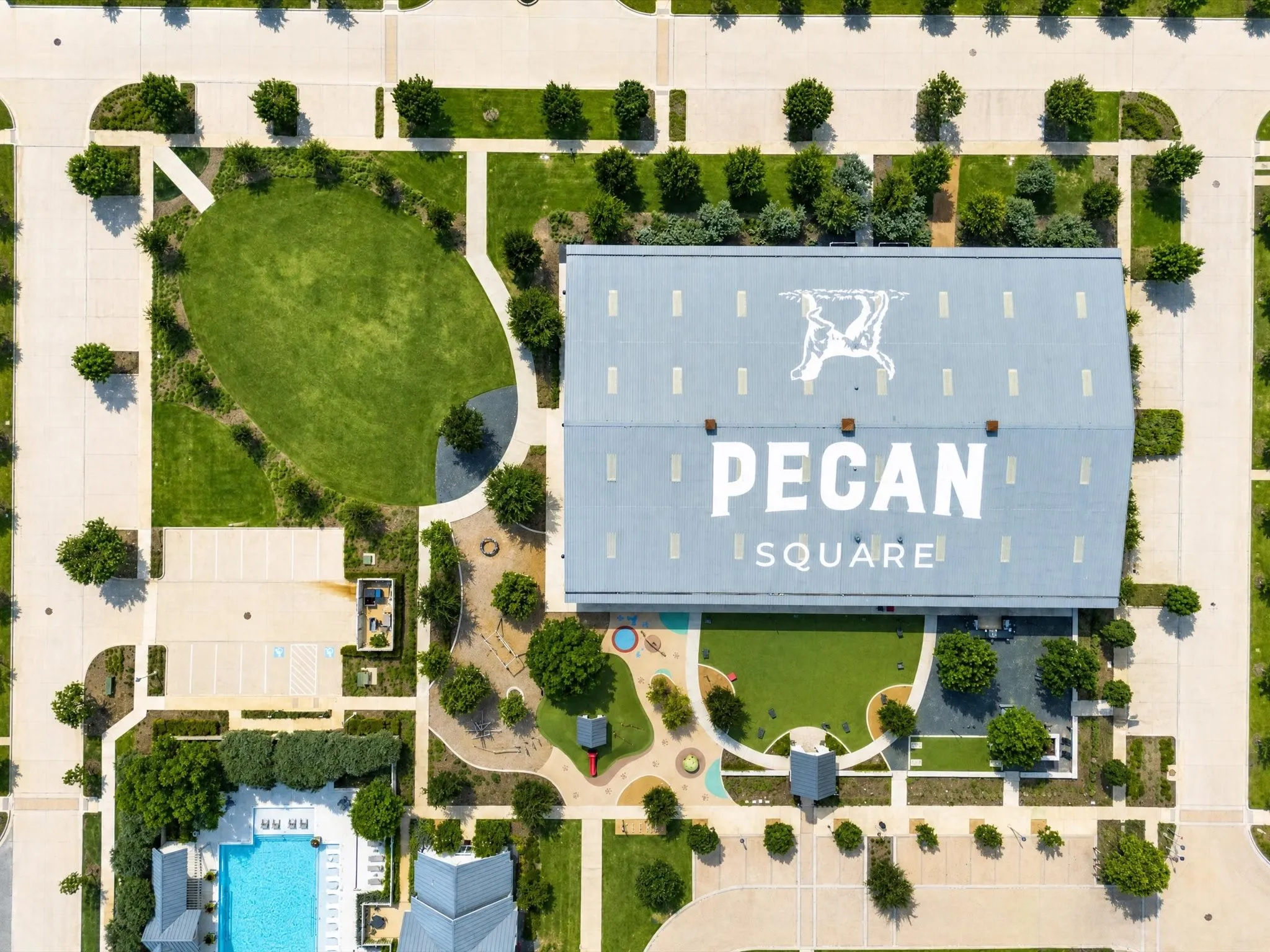 Aerial perspective showcasing a large commercial structure with "Pecan Square" branding, surrounded by extensive green spaces