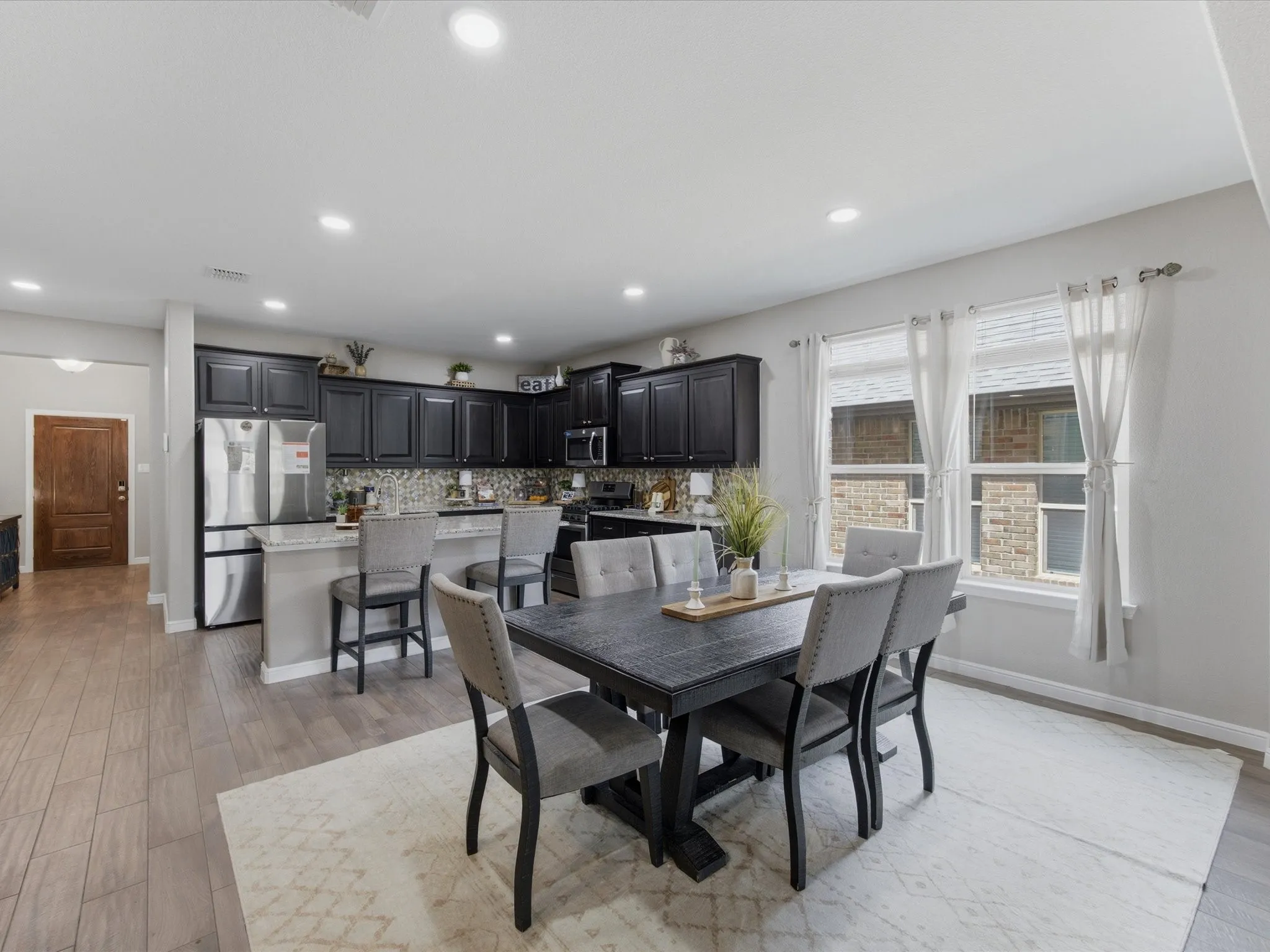 Open-concept kitchen and dining area featuring dark cabinetry, stainless steel appliances, a breakfast bar with stone-finish countertops, and recessed lighting