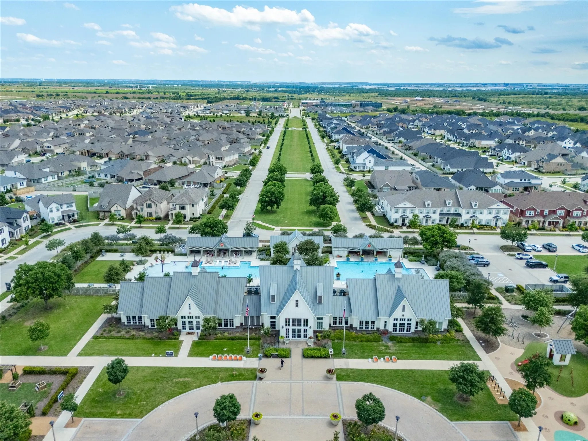 Expansive community recreation center featuring multiple pools, a large clubhouse with a metal roof, and surrounding green spaces