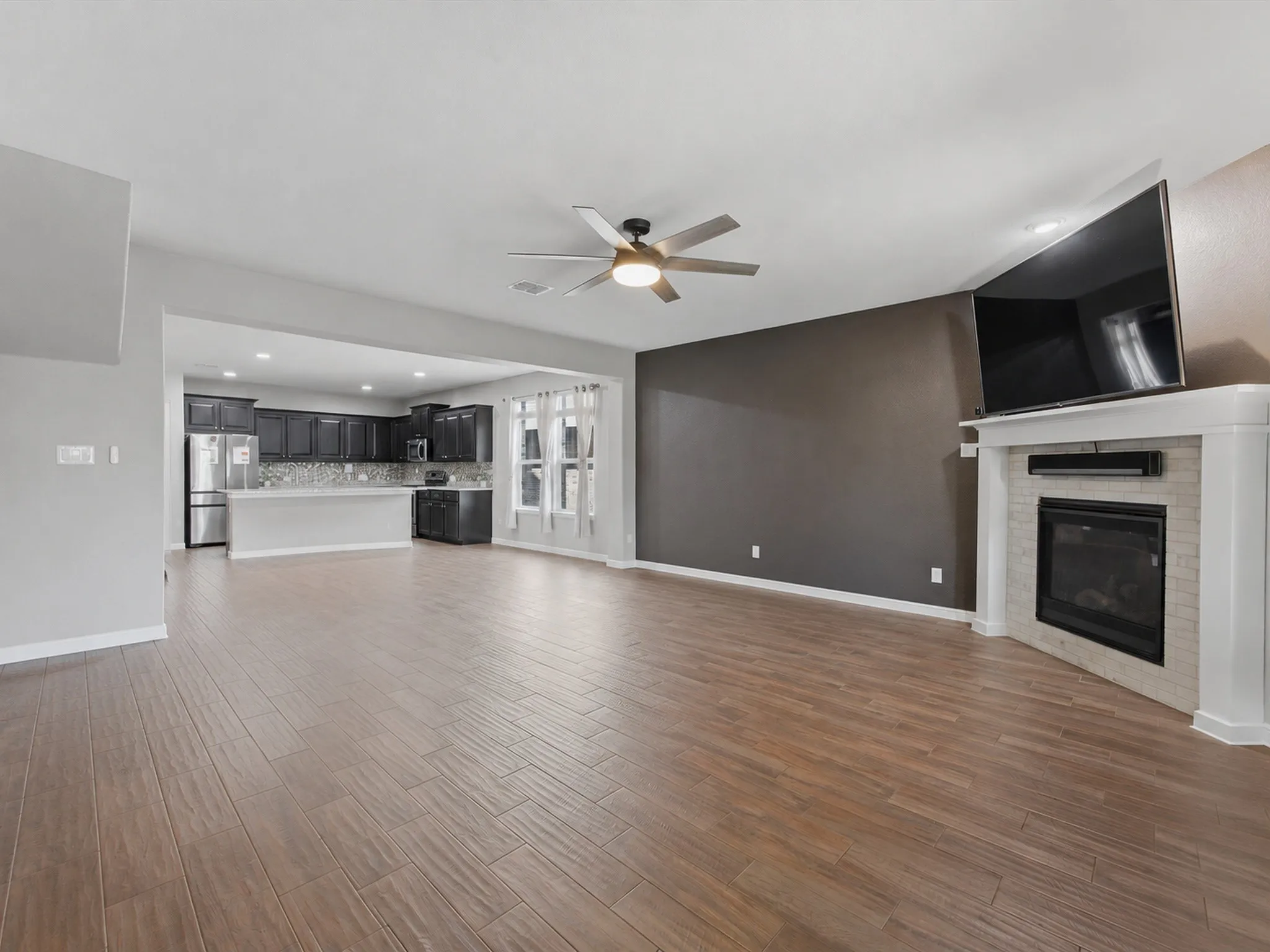 Virtually removed furniture, in Open-concept living space featuring wood-finish flooring, a contemporary ceiling fan, and a fireplace with a tiled surround
