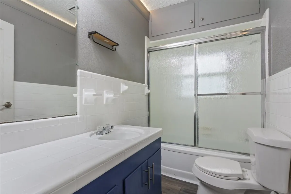Bathroom featuring a tile-top vanity with blue cabinetry, white subway tile wainscoting, and a shower with frosted sliding doors