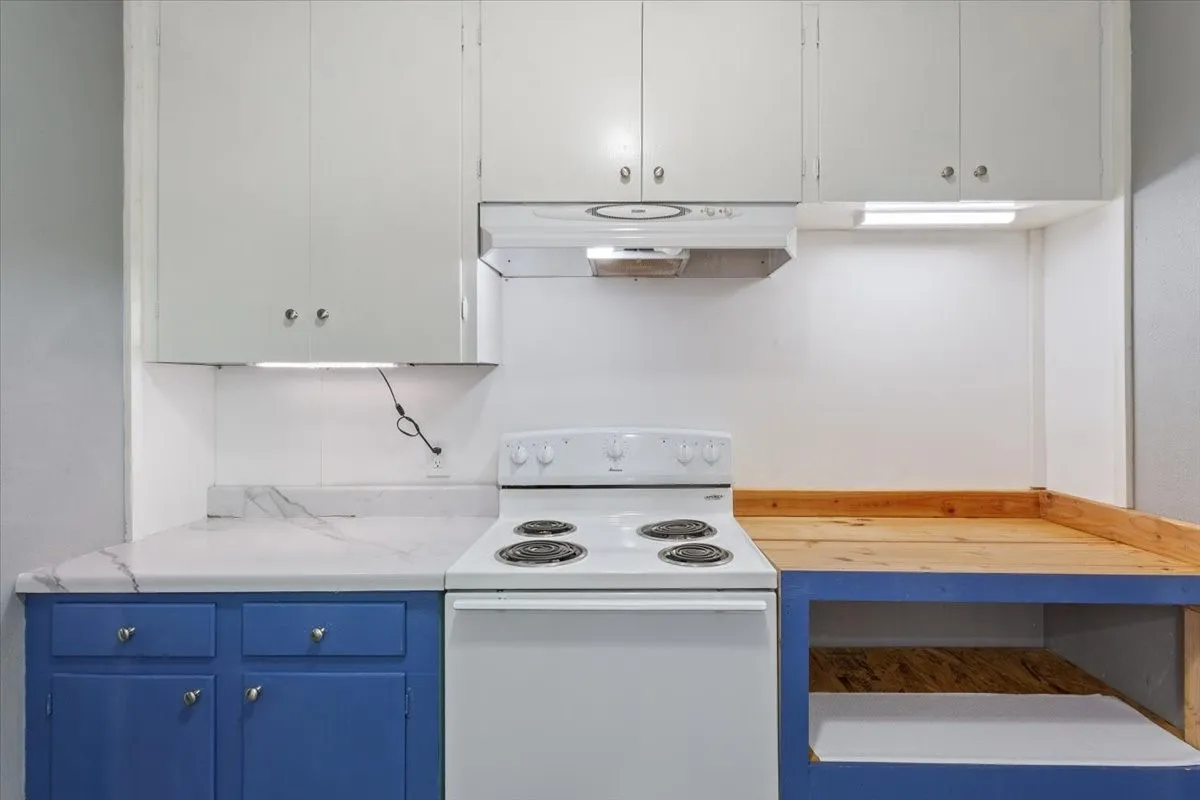 Kitchen featuring white upper cabinetry, blue lower cabinetry, white electric range, and a white range hood