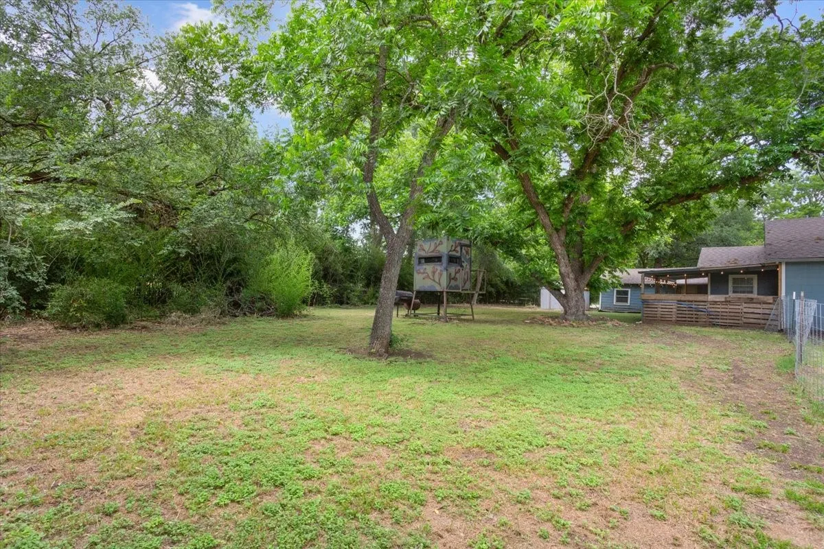 Spacious yard featuring mature trees, a wooden deck with slatted fencing, and a wire perimeter fence