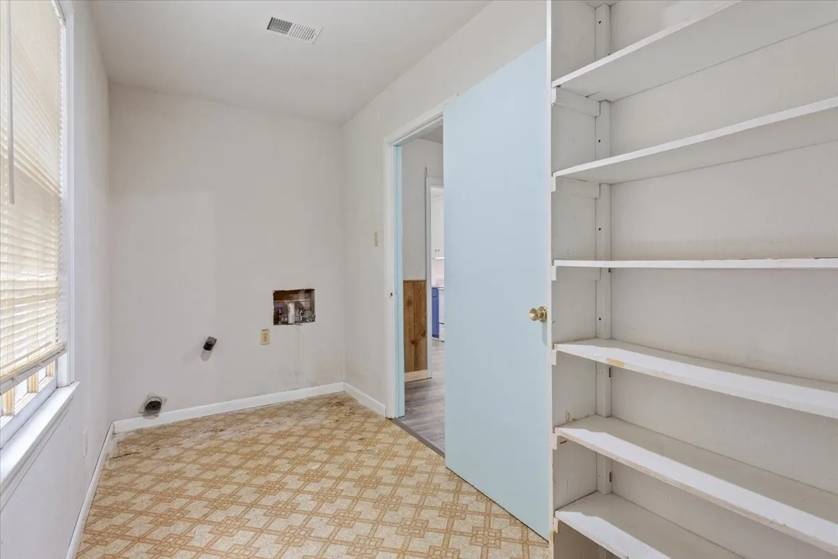 Utility room featuring a window with blinds, wall hookups, and a built-in shelving unit