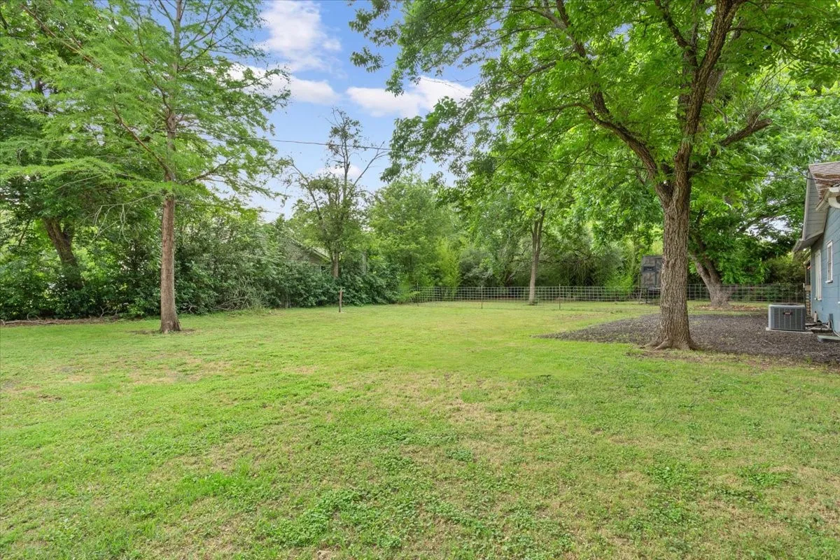 Expansive green lawn with mature trees and a partial wire fence
