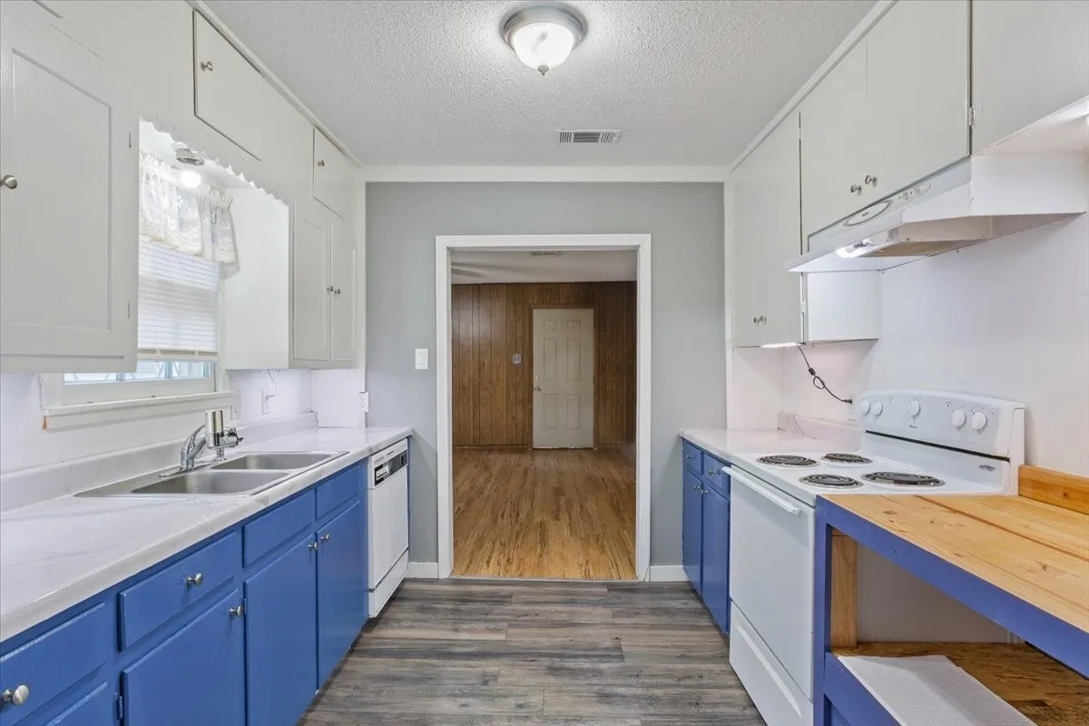 Galley kitchen featuring dual-tone cabinetry, white countertops, and wood-finish flooring