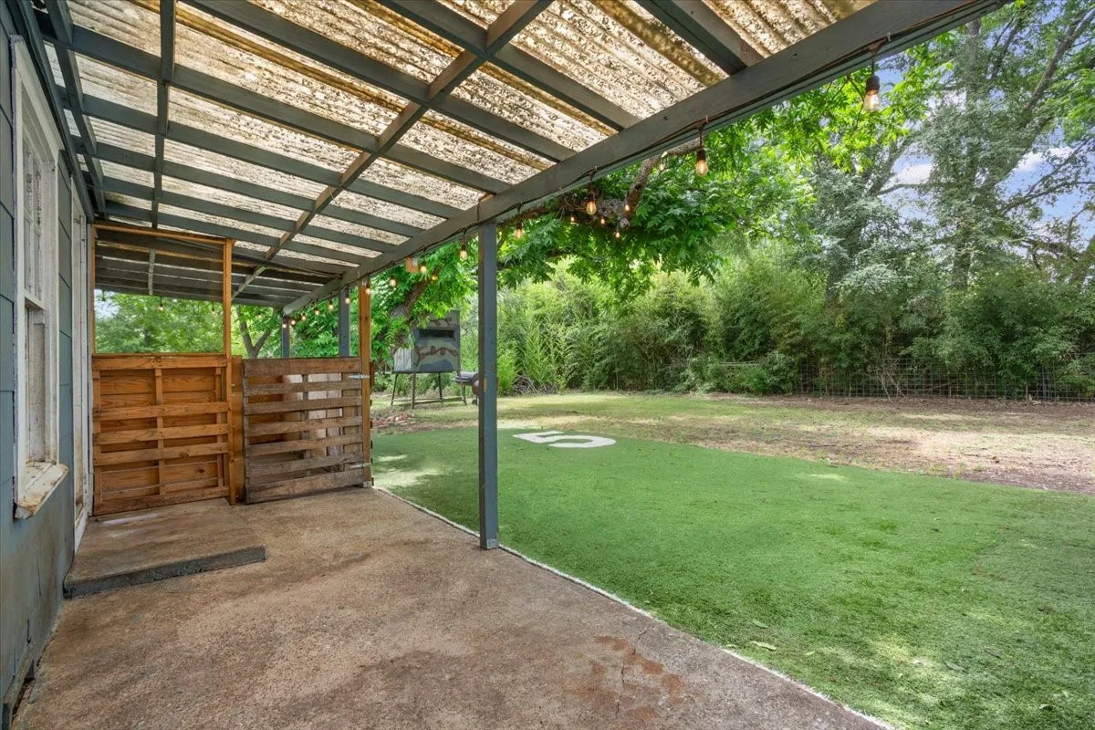 Covered patio with concrete flooring, featuring a translucent corrugated roof and string lighting