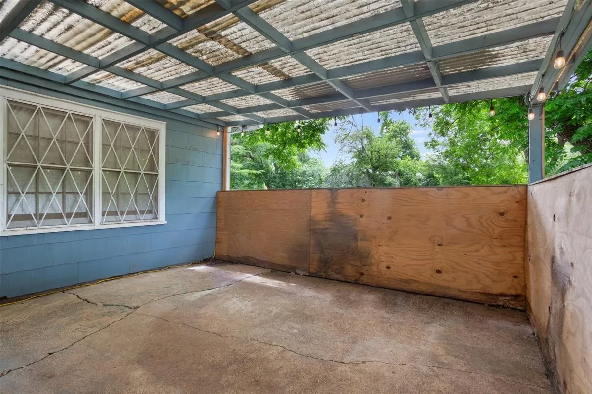 Covered patio space featuring a translucent corrugated roof, perimeter string lighting, and a partial privacy wall