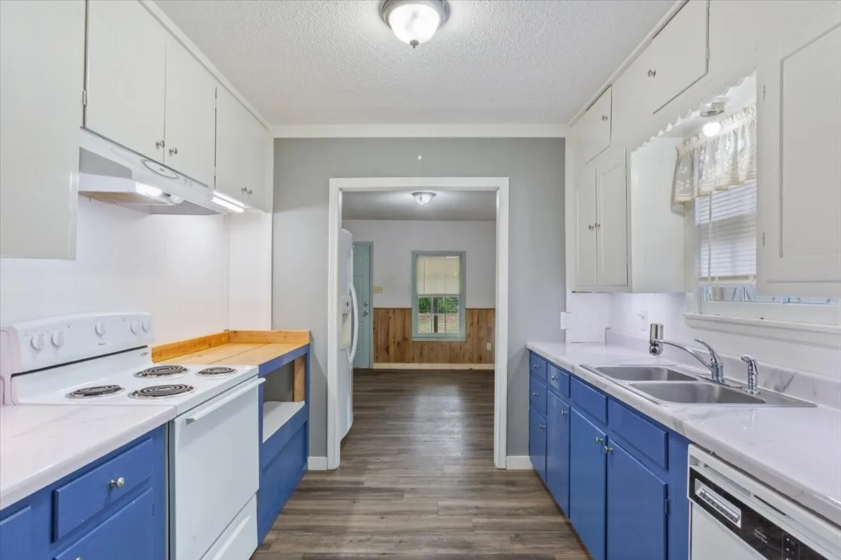 Galley kitchen featuring white upper cabinetry, vibrant blue lower cabinetry, and wood-finish flooring