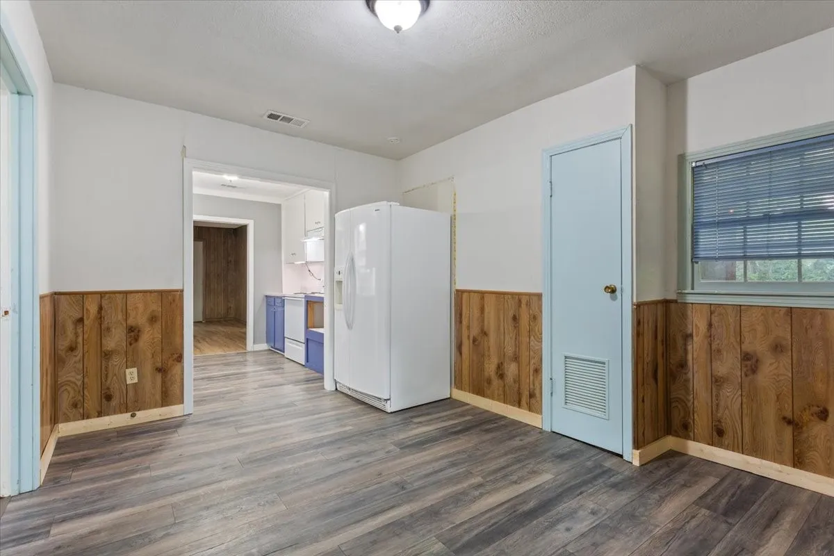 Spacious room featuring wood-finish flooring, half-wall wood paneling, and a light blue painted door