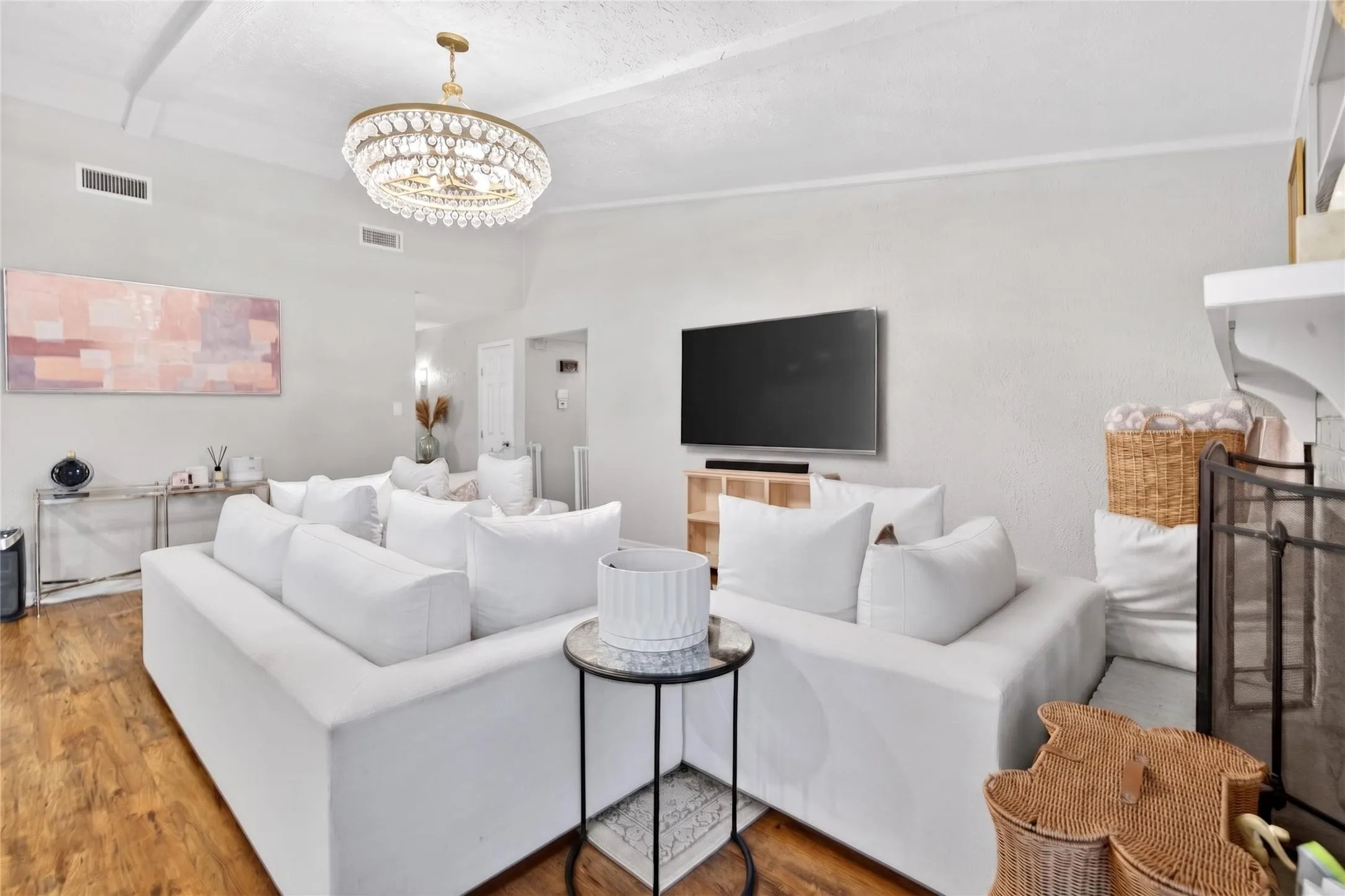 Living area featuring wood-finish flooring, a decorative chandelier, recessed air vents, a wall-mounted television, and a built-in fireplace mantel with shelving
