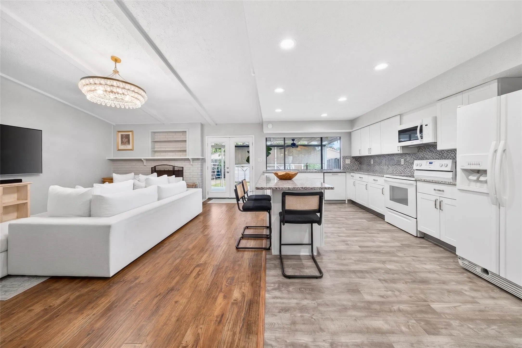 Open-concept living area and kitchen featuring wood-finish flooring, a contemporary chandelier, a fireplace with built-in shelving, white cabinetry, and a patterned backsplash