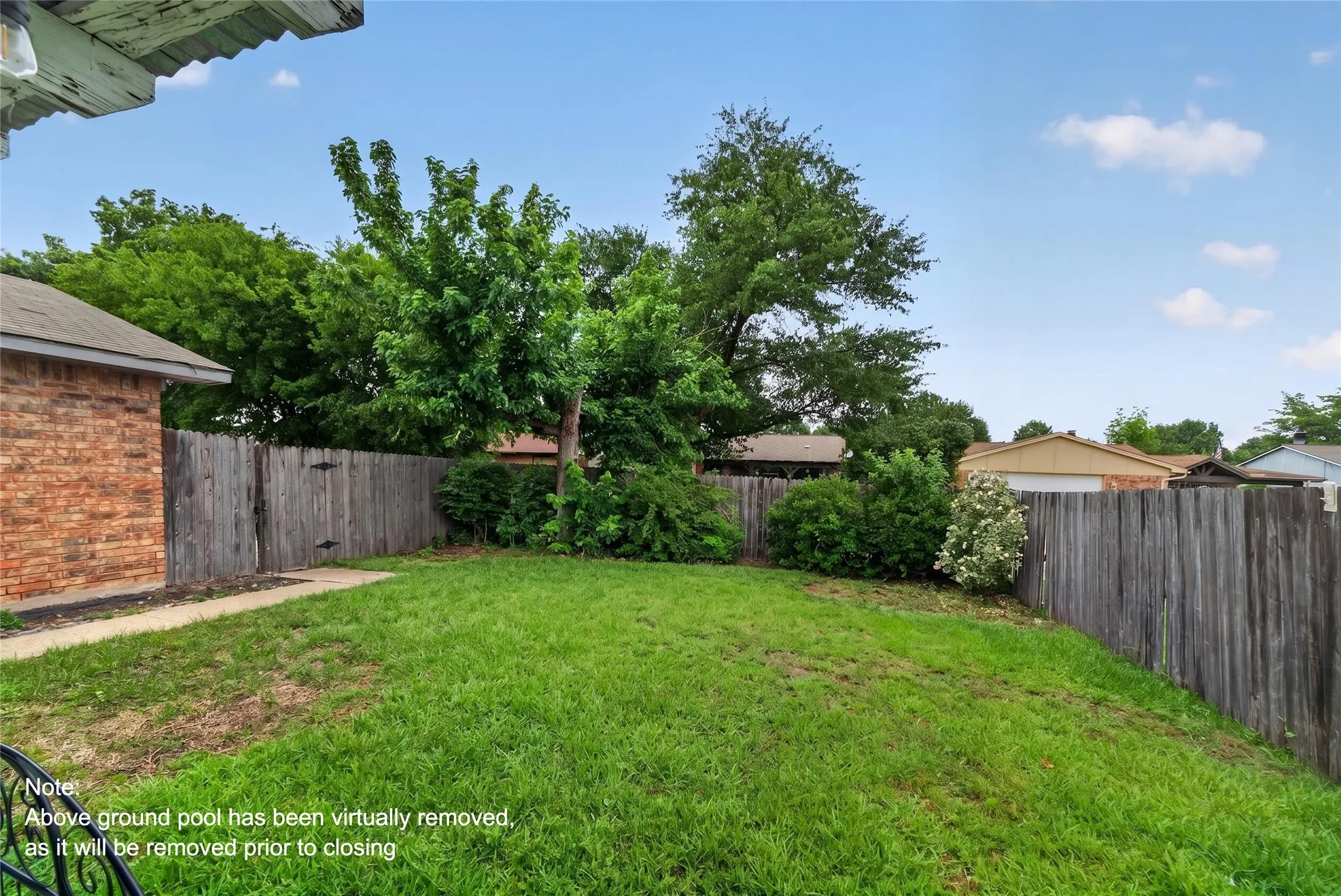 Expansive backyard featuring a natural wood privacy fence, mature trees, and a concrete walkway leading to the brick exterior of the property