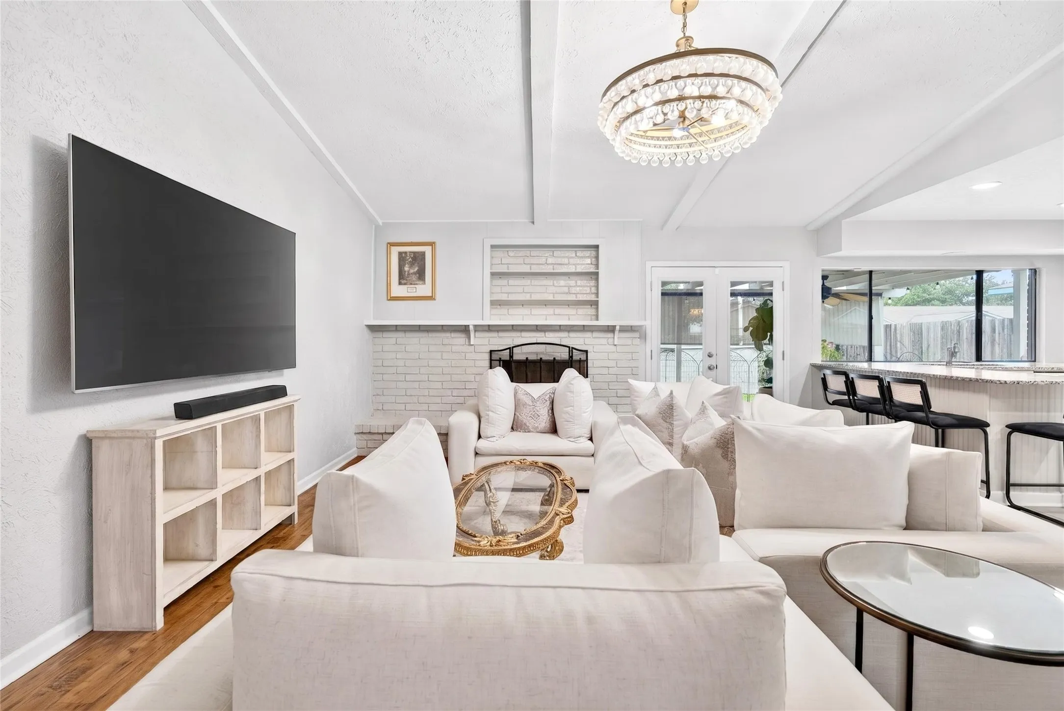 Living area featuring a white brick fireplace with mantel, exposed ceiling beams, and wood-finish flooring