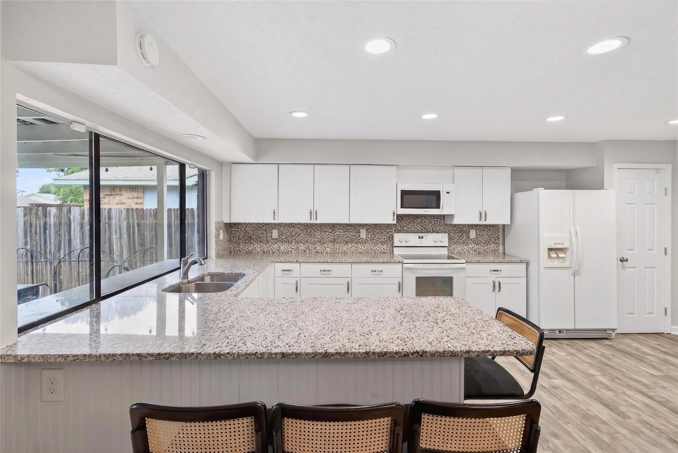 Kitchen featuring white cabinetry, speckled countertops, stainless steel sink, tile backsplash, and wood-finish flooring