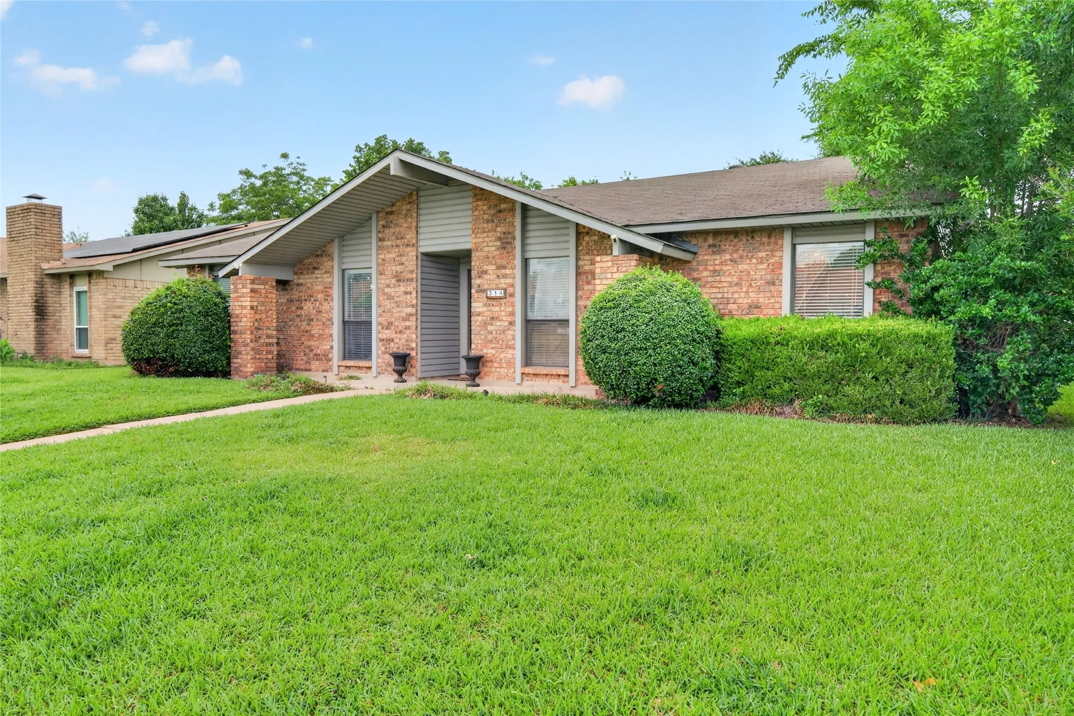 Brick exterior featuring an A-frame entry, prominent chimney, and a well-maintained lawn with mature shrubbery and trees