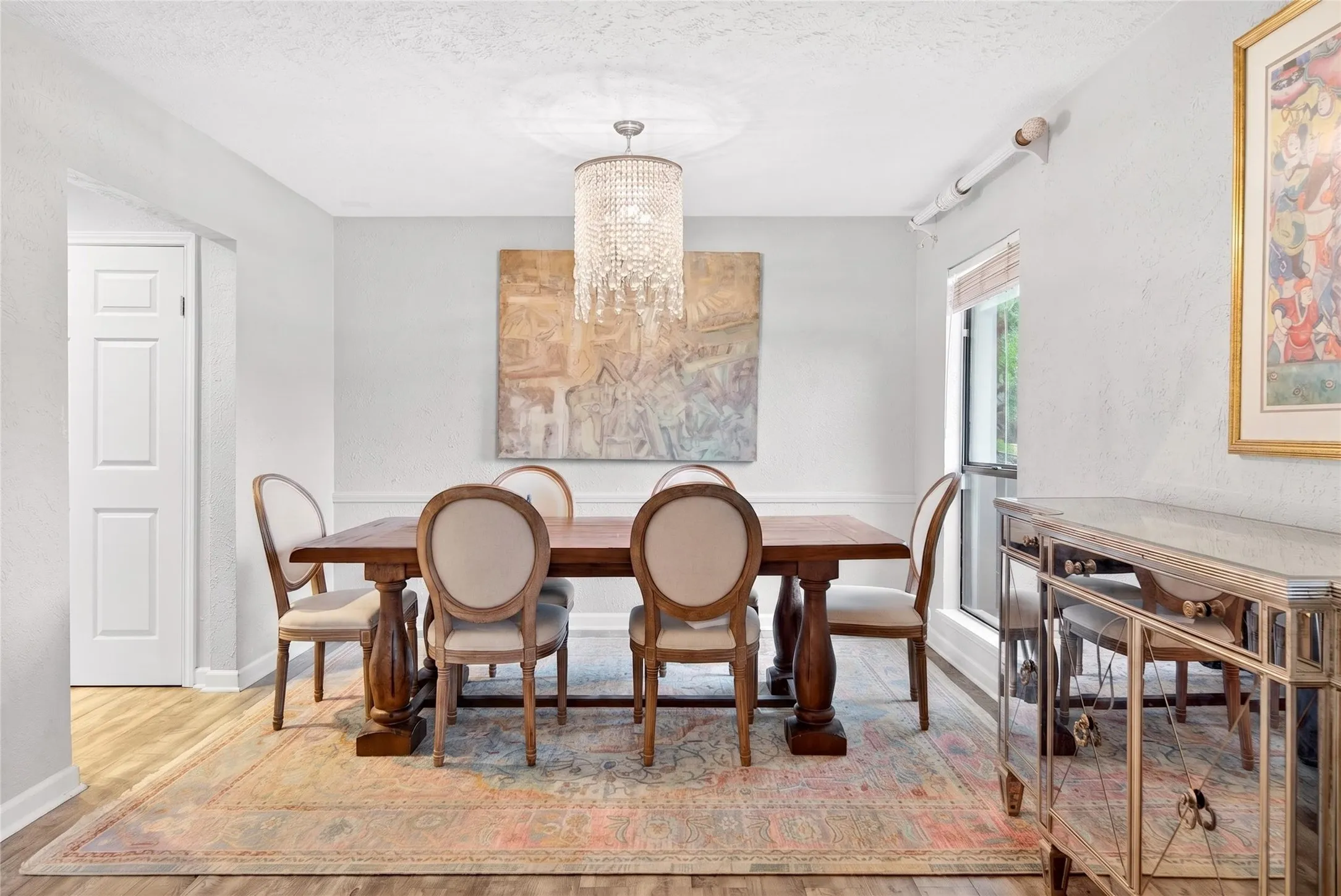 Formal dining space featuring a crystal chandelier, wood-finish flooring, white paneled door, and a window with a wood blind