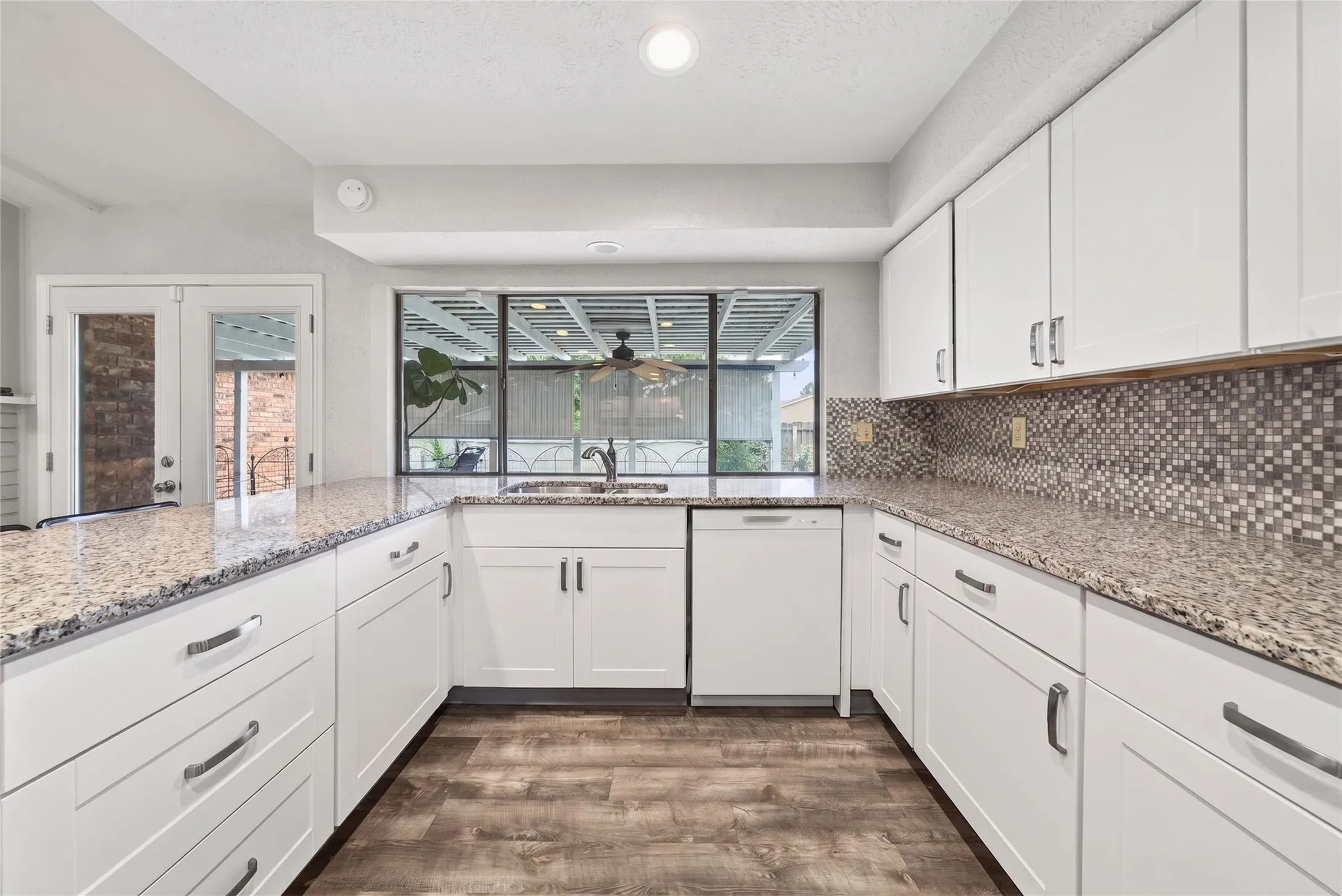 Kitchen featuring white cabinetry, granite countertops, a mosaic tile backsplash, wood-finish flooring, and a window overlooking an outdoor screened area