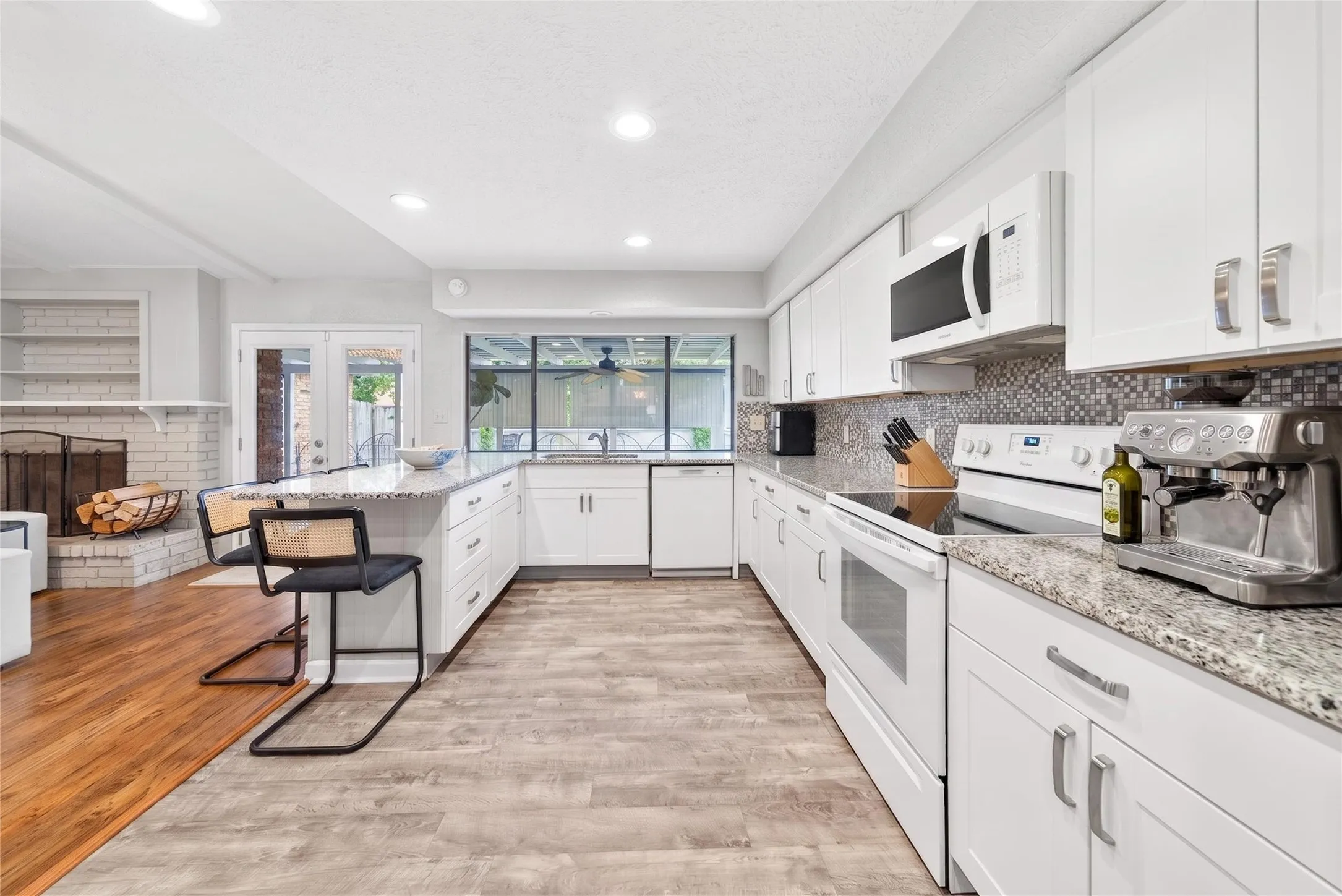 Spacious kitchen featuring white cabinetry, light-colored granite countertops, and a mosaic tile backsplash