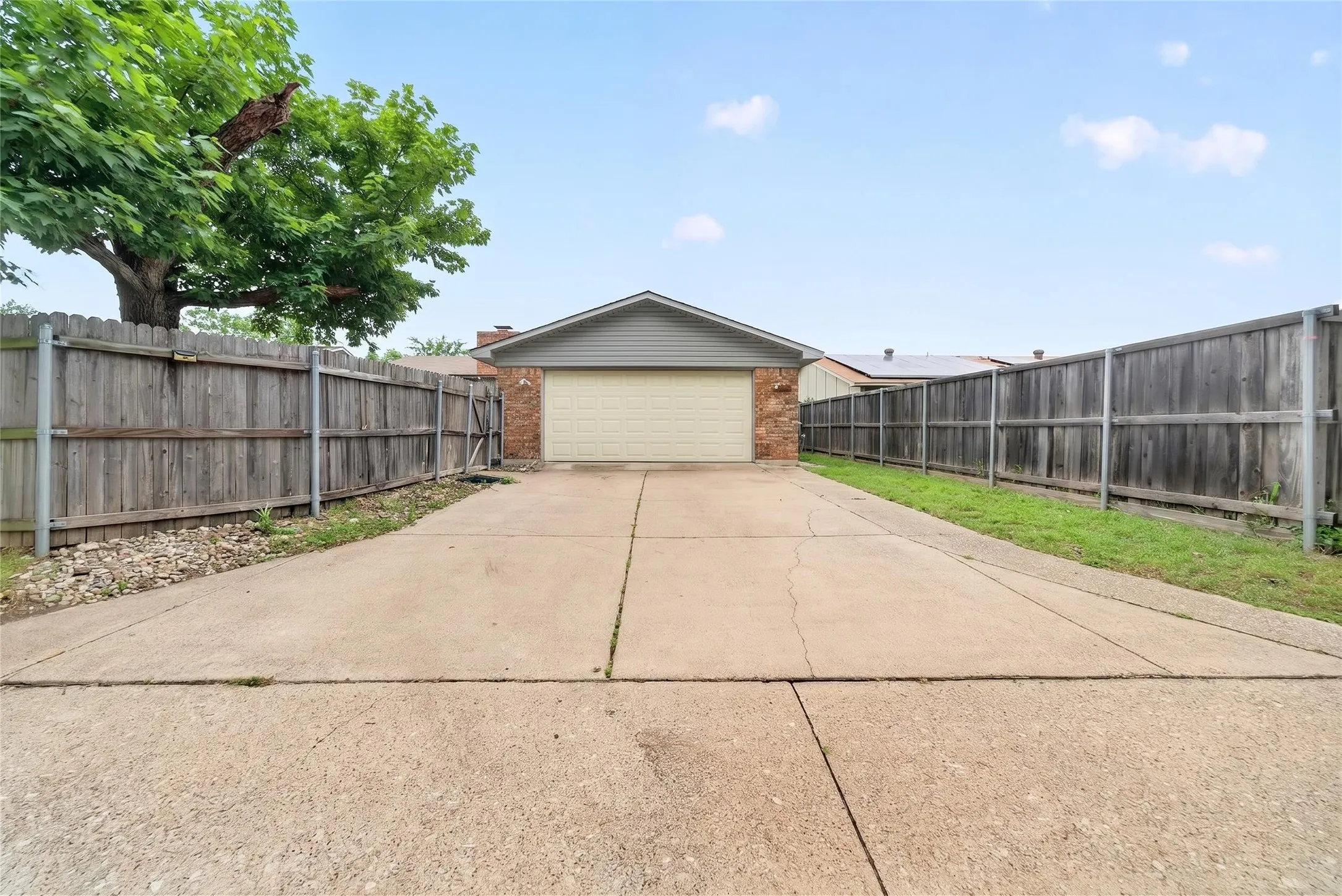 Two-car garage with brick siding and a long concrete driveway, bordered by wooden privacy fencing