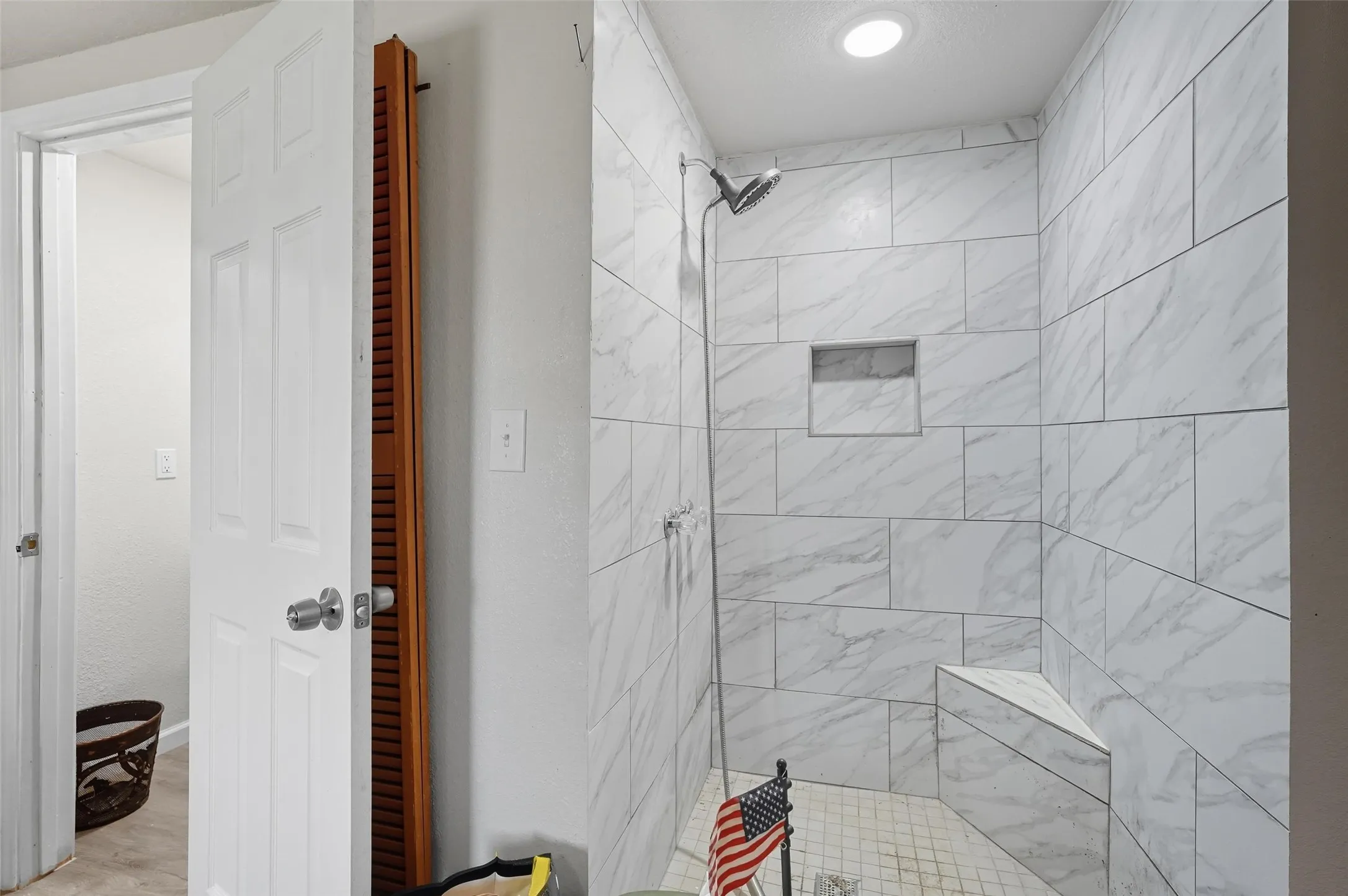 Walk-in shower featuring large format wall tiles, built-in shower niche, integrated corner bench, and a tiled shower pan
