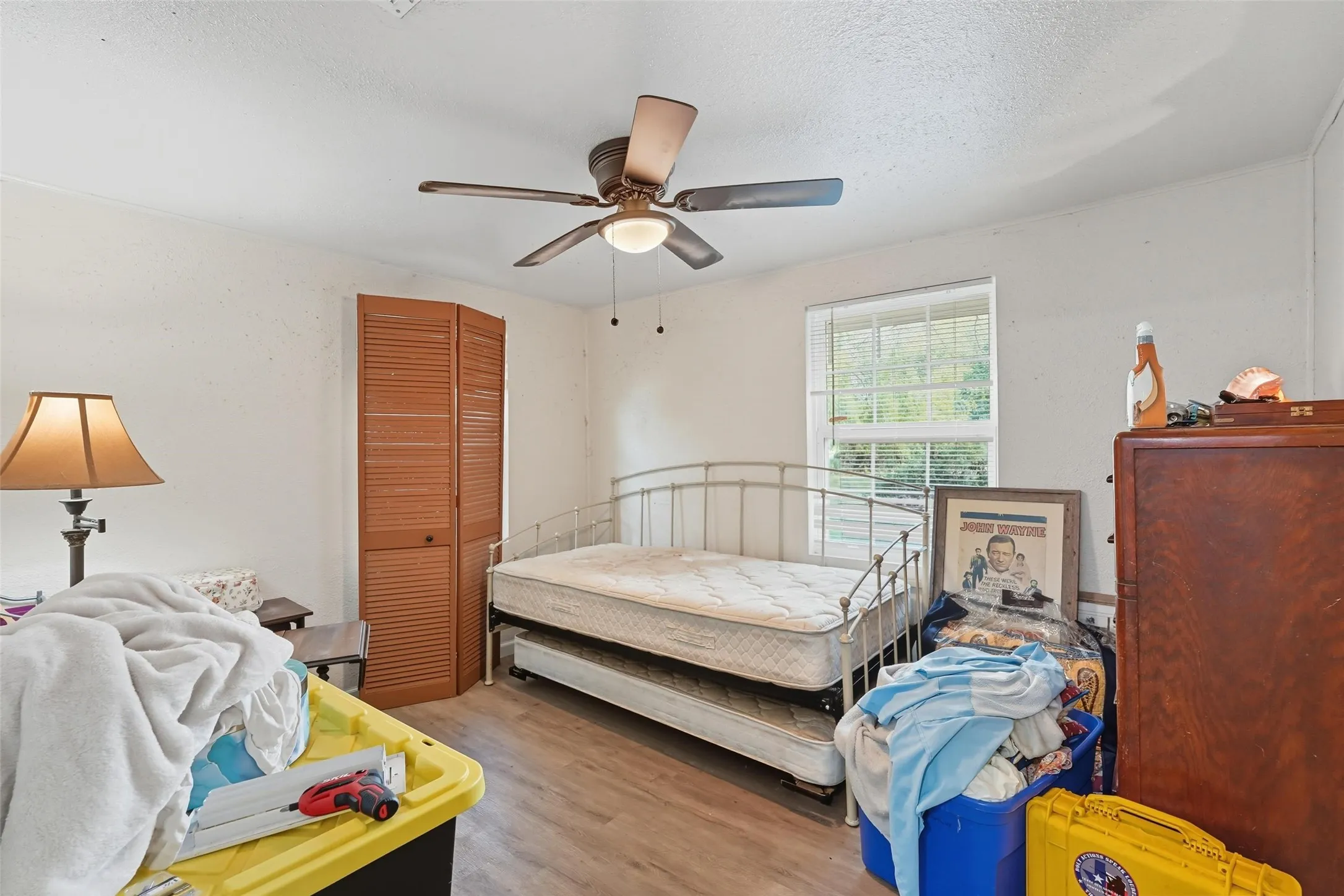 Room with wood-finish flooring, a window with blinds, and a built-in closet with louvered bi-fold doors