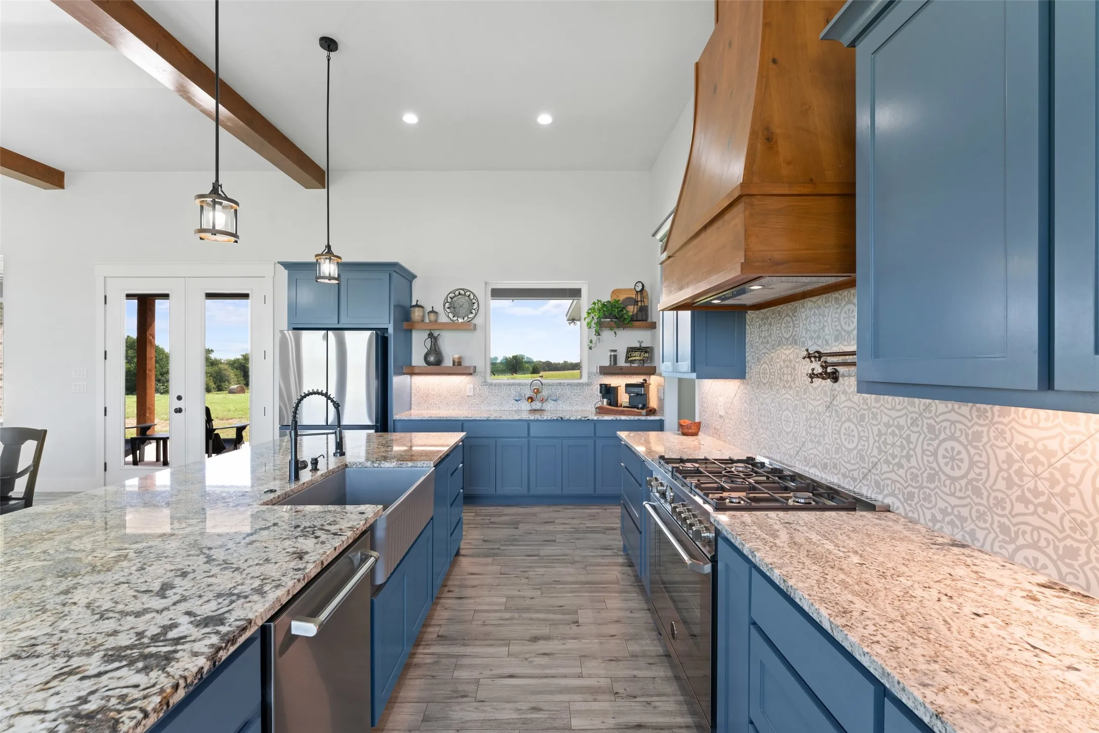 Gourmet kitchen featuring blue cabinetry, granite countertops, a farmhouse sink, stainless steel appliances, and a wood range hood