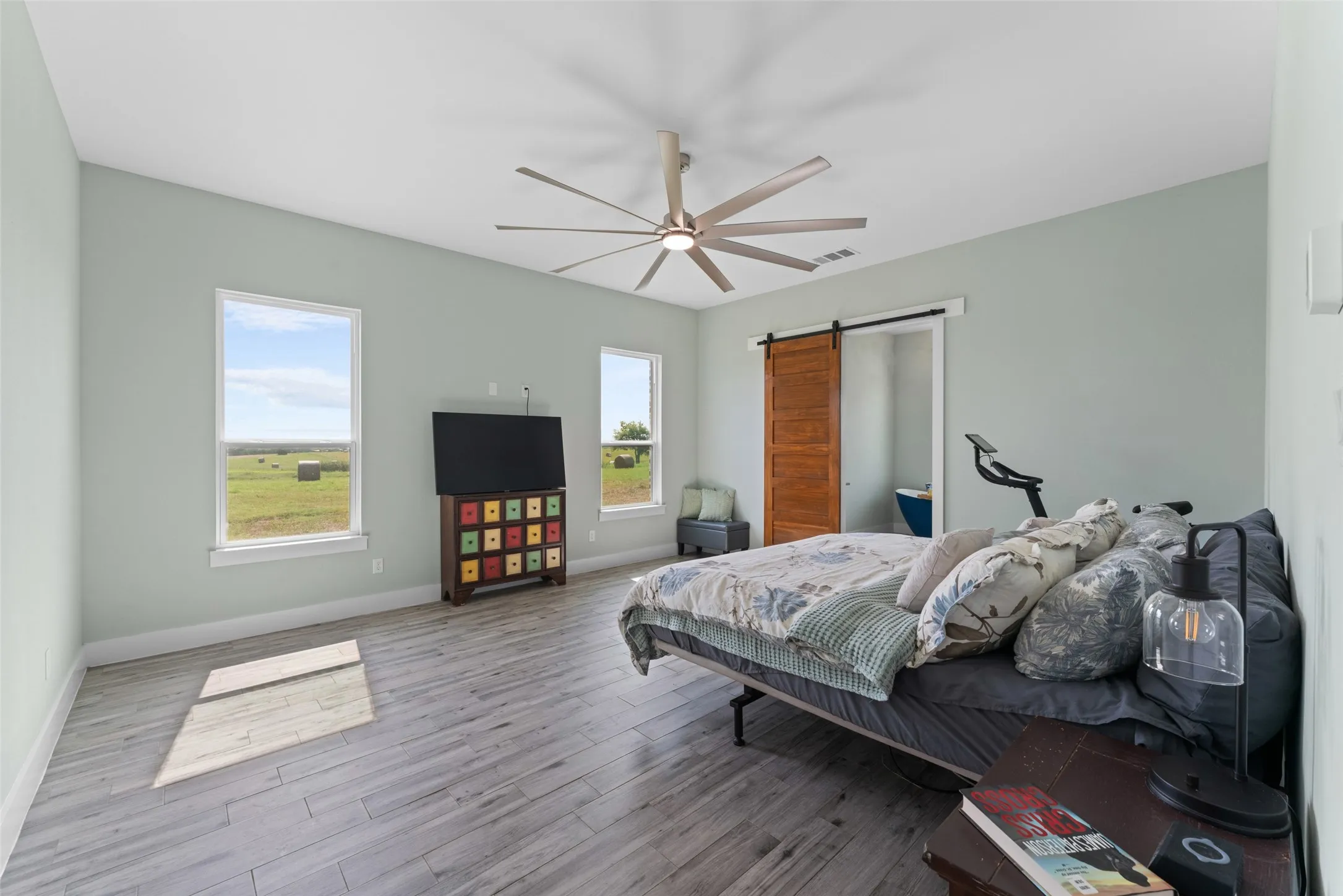 Spacious room featuring wood-finish flooring, two windows, and a large ceiling fan with integrated lighting