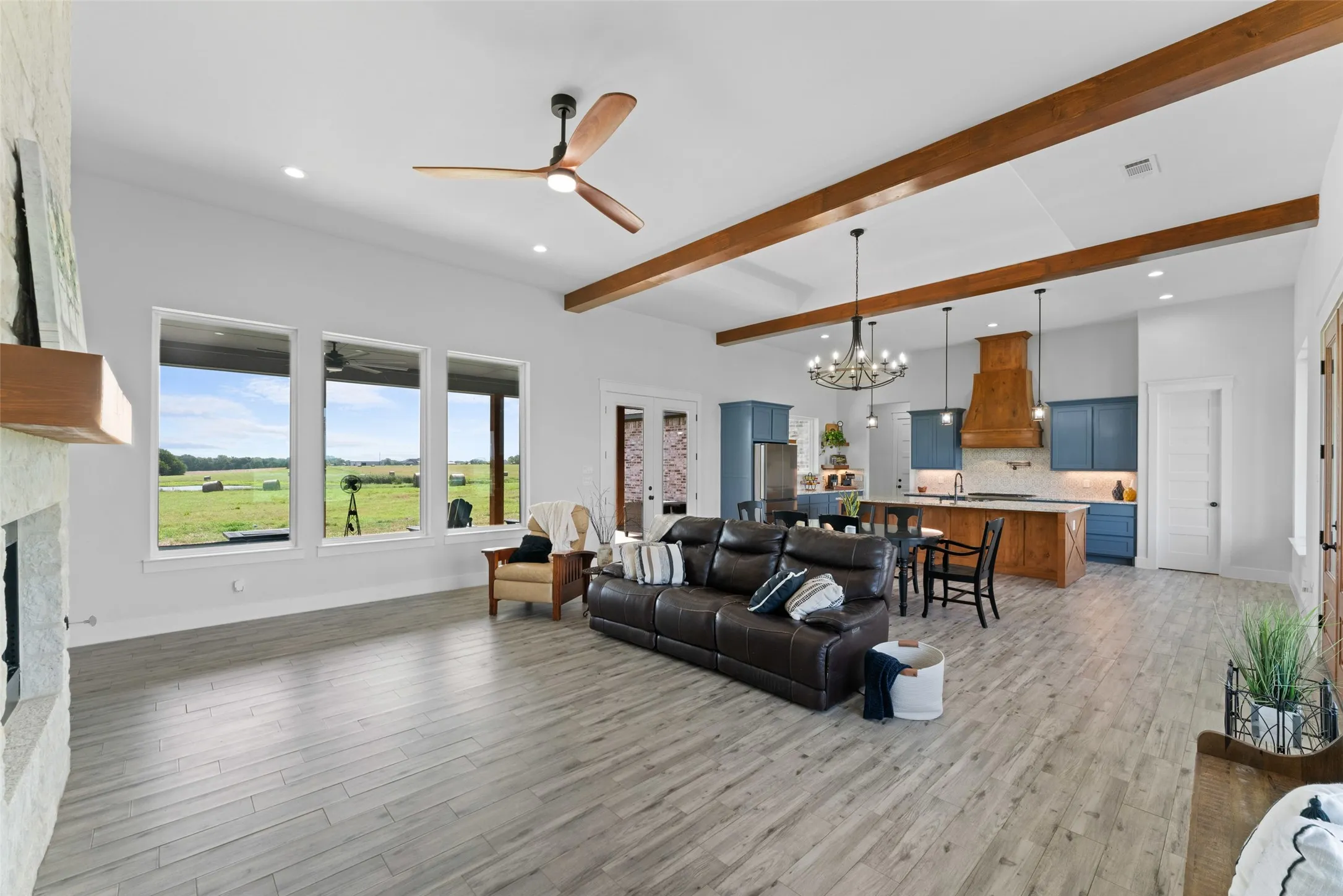 Spacious living area featuring wood-finish flooring, exposed ceiling beams, and a stone-clad fireplace