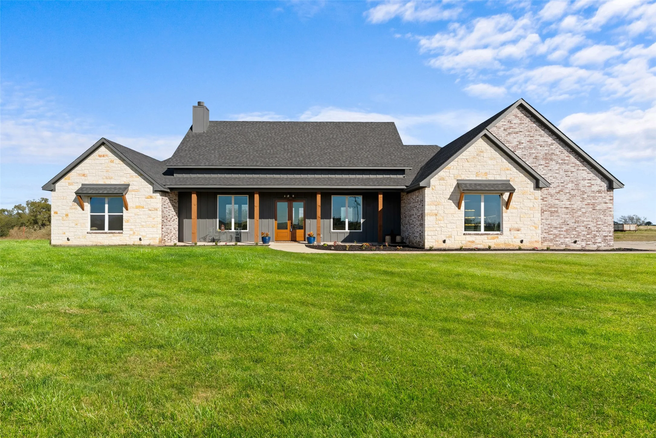 Expansive front lawn complementing a stone and brick façade home with a dark gray shingle roof