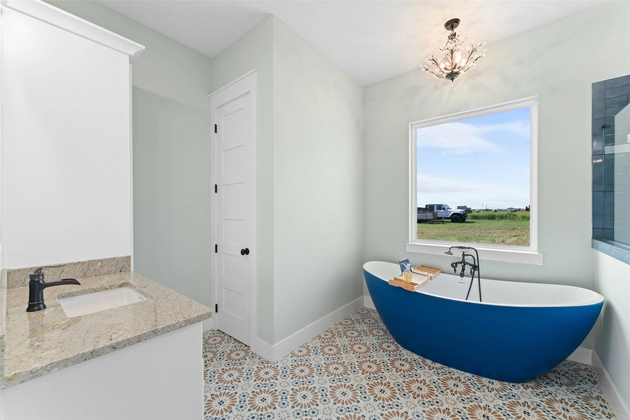Freestanding blue soaking tub with floor-mounted faucet, complemented by patterned floor tiles