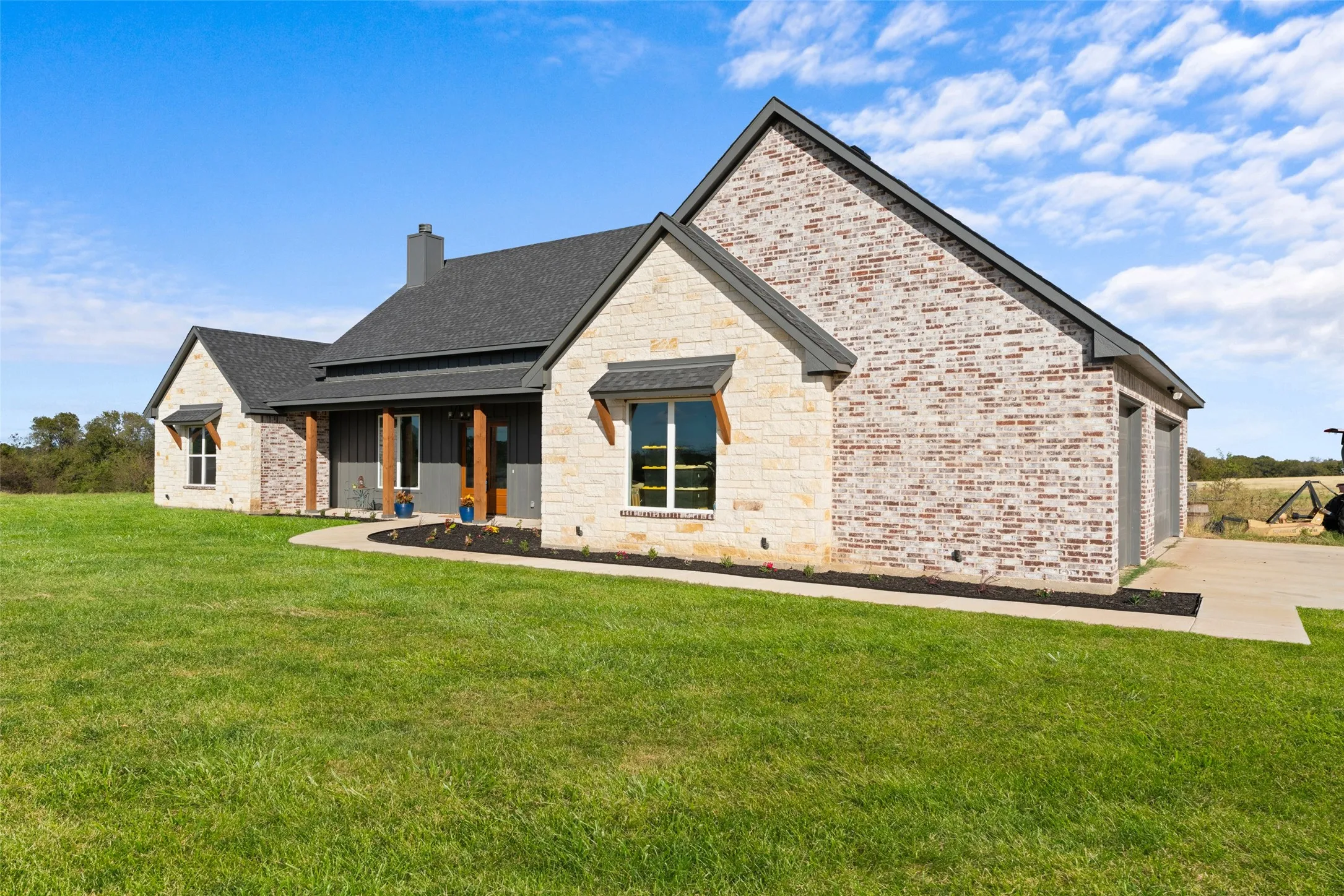 Exterior featuring a blend of light-colored brick and stone, a dark gray shingle roof, and a covered porch with natural wood posts
