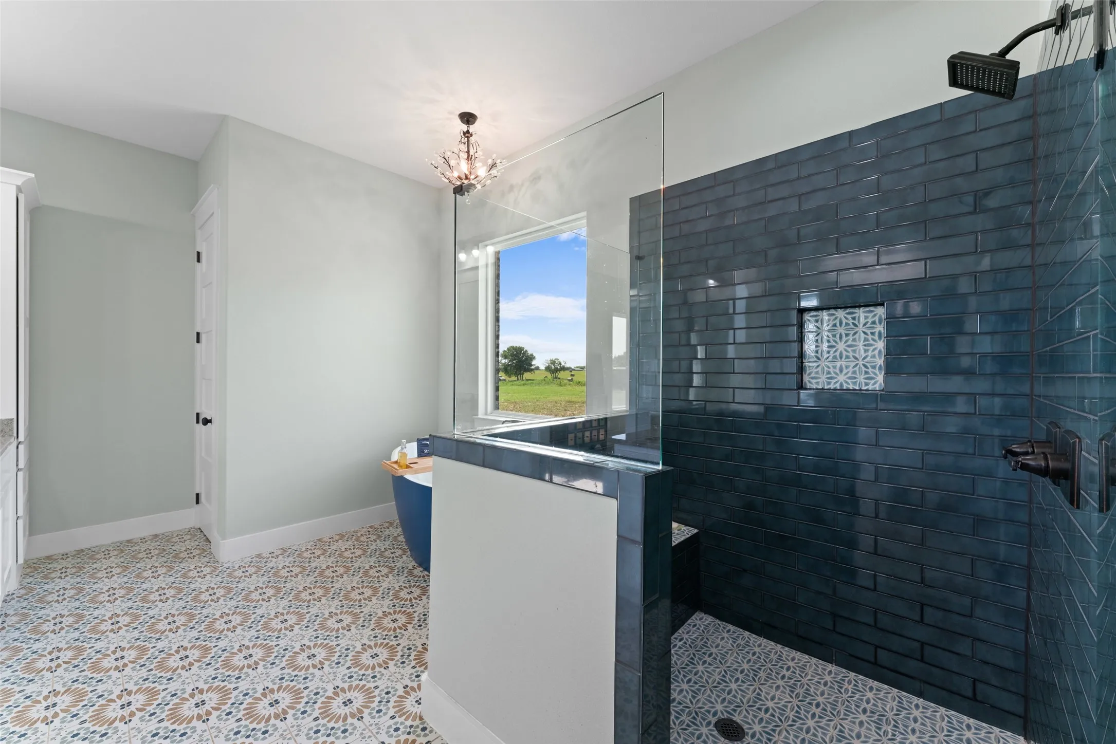 Spacious bathroom featuring patterned floor tiling, a walk-in shower with dark blue subway tile, a built-in shower niche, and a freestanding soaking tub