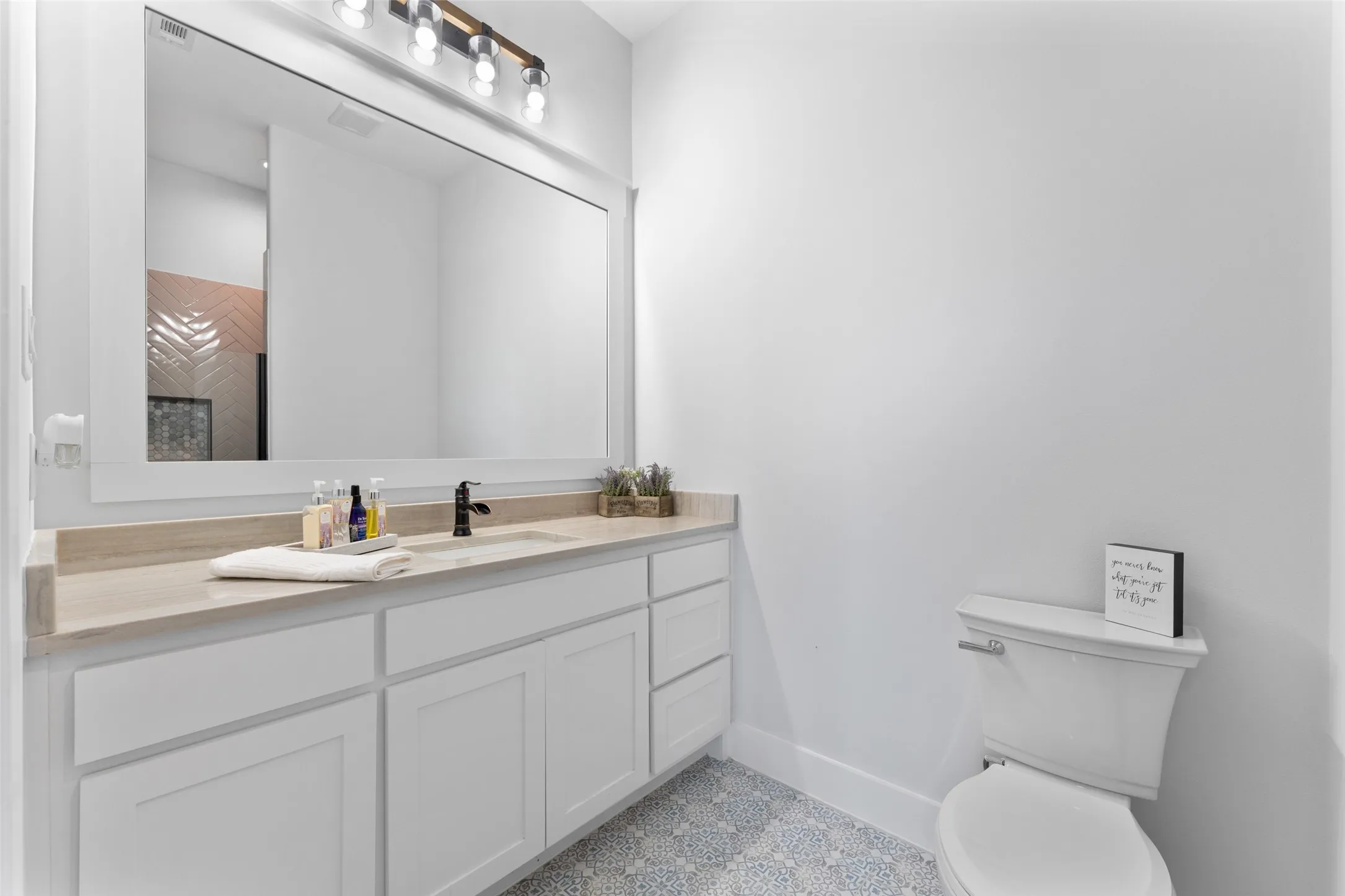 Bathroom featuring a white shaker-style vanity with ample storage, light-toned countertop, rectangular undermount sink, and matte black faucet