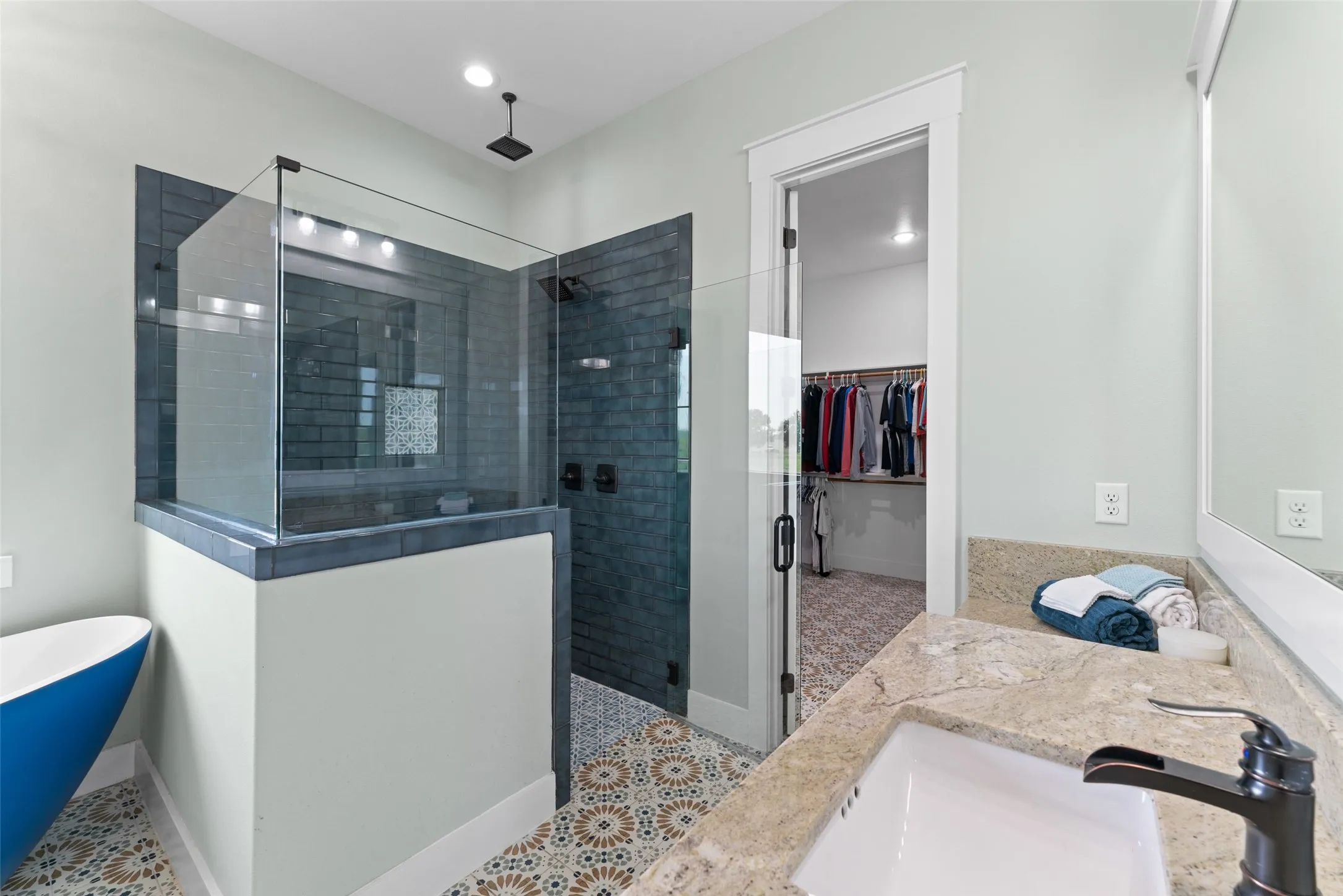 Bathroom featuring a walk-in shower with glass enclosure, blue subway tile, and a rainfall showerhead