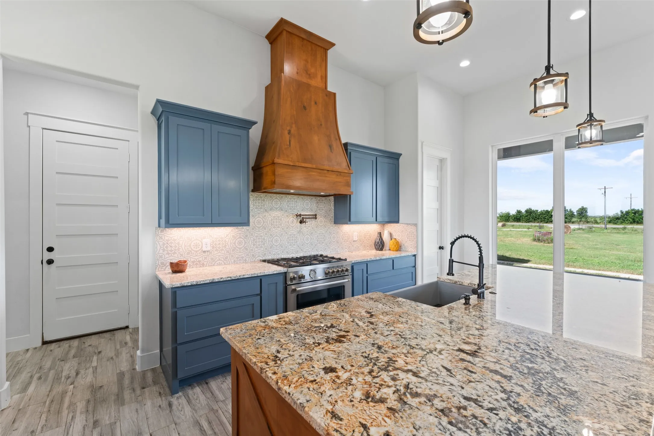 Kitchen featuring a large central island with granite countertop, blue cabinetry, a wood-finish range hood, stainless steel gas range, and large windows