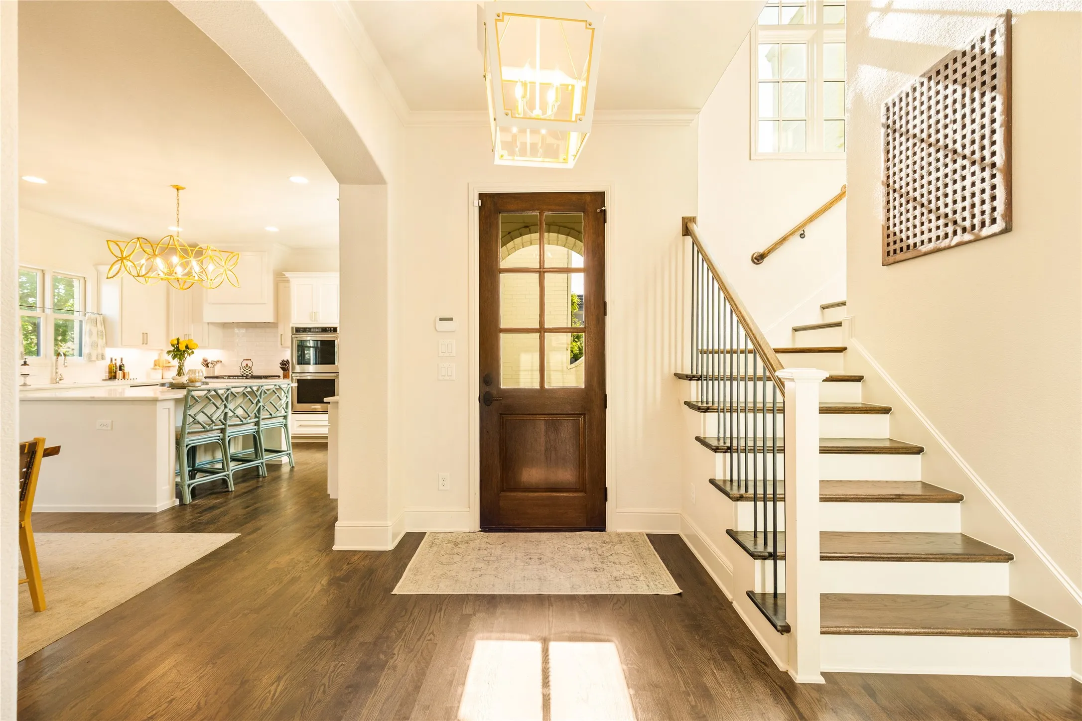 Bright and welcoming entryway showcases rich wood flooring, elegant arched details, and a striking staircase with classic iron balusters. Natural light pours through oversized windows and the glass paneled front door, creating a warm and sophisticated first impression.