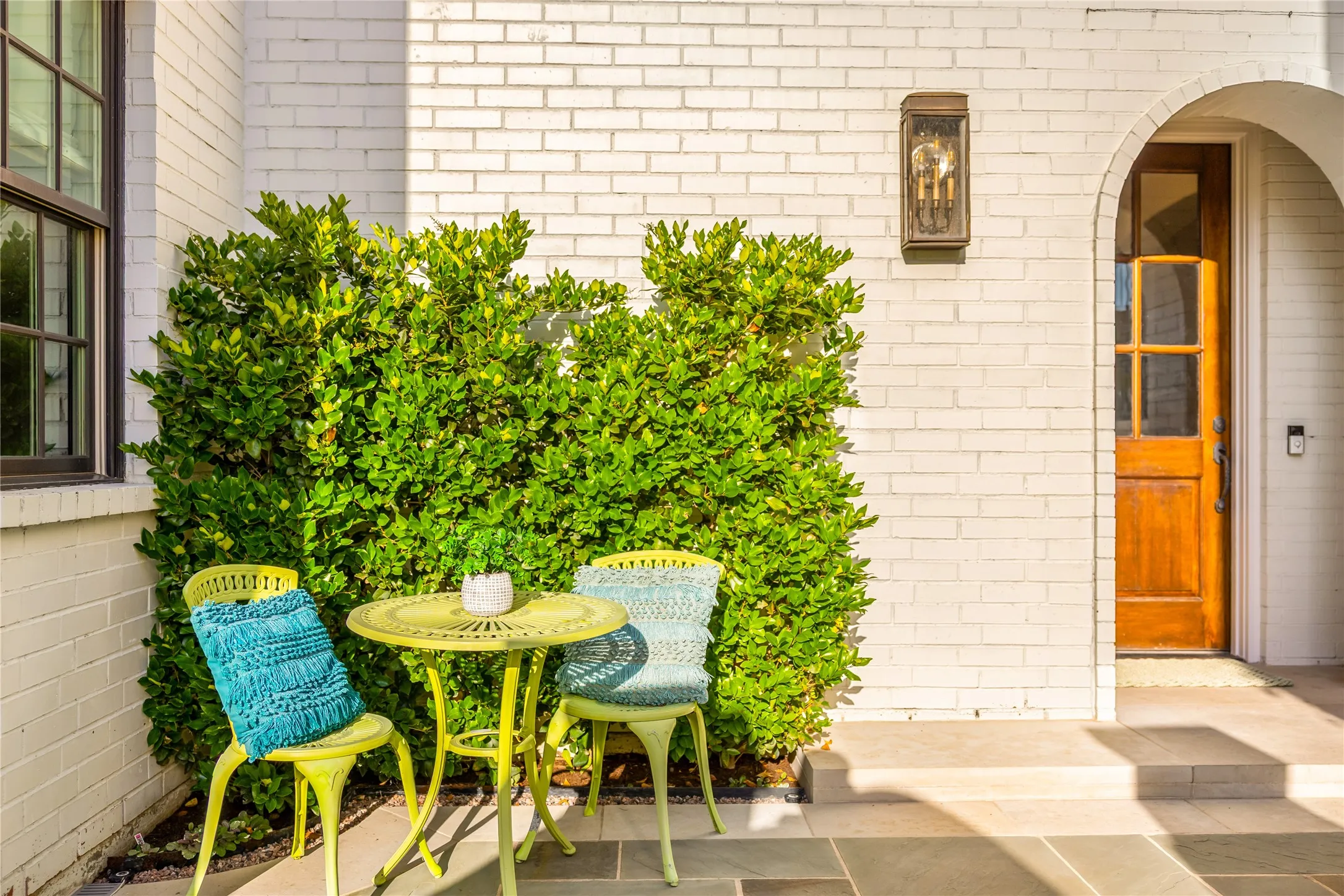 Charming front patio nook offers the perfect spot for morning coffee or evening conversation, framed by lush greenery and warm architectural details. The inviting entryway and intimate outdoor seating create a welcoming blend of comfort and style.