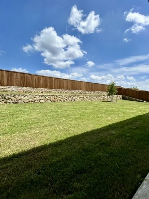 Expansive backyard featuring a lush lawn, a mature wood privacy fence, and a decorative stone retaining wall