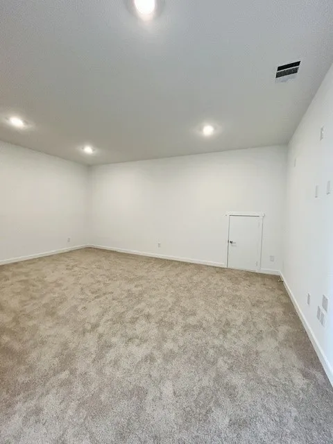 Spacious room with new carpeting, crisp white walls, recessed ceiling lighting, and a white interior door