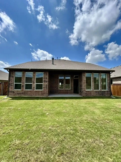 Expansive green lawn backing a brick exterior featuring multiple windows and a covered concrete patio