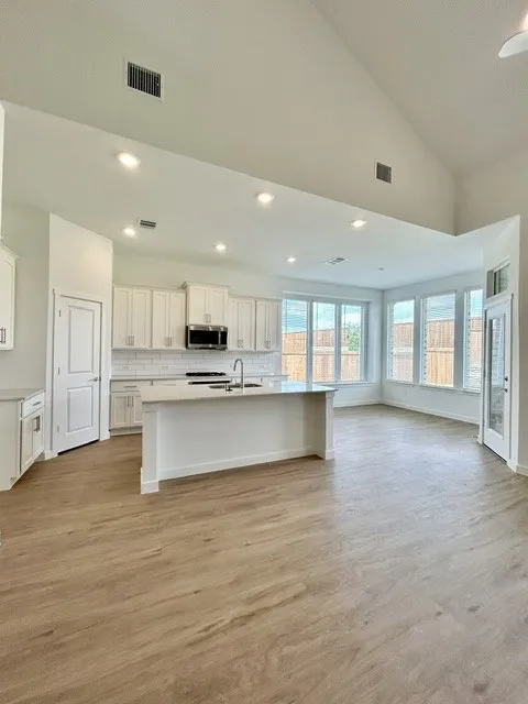 Modern kitchen and living area featuring wood-finish flooring, vaulted ceilings, and recessed lighting