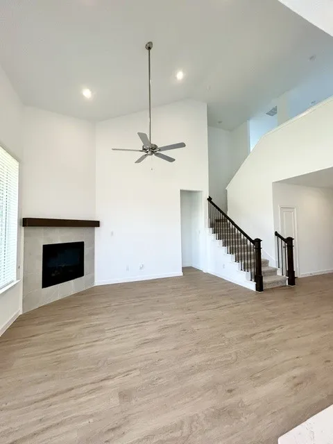 Spacious room featuring vaulted ceilings, wood-finish flooring, a contemporary fireplace with a tiled surround and wood mantel, and a staircase with dark wood newel posts and metal balusters