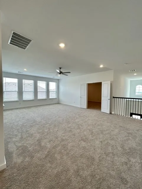 Spacious carpeted room featuring multiple windows, recessed lighting, and a ceiling fan
