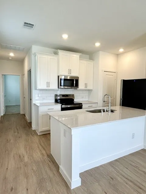 Modern kitchen featuring white shaker cabinetry, stainless steel appliances, a subway tile backsplash, and a large island with a composite countertop and undermount sink