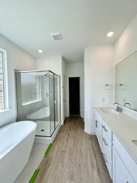 Modern bathroom featuring a freestanding soaking tub, glass-enclosed shower, dual-sink vanity with quartz countertop, and wood-finish flooring
